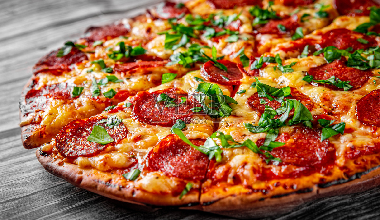 意大利辣香肠披萨配马苏里拉芝士，意大利腊肠，番茄酱，胡椒，香料和新鲜罗勒。木桌子上的意大利披萨照片摄影图片
