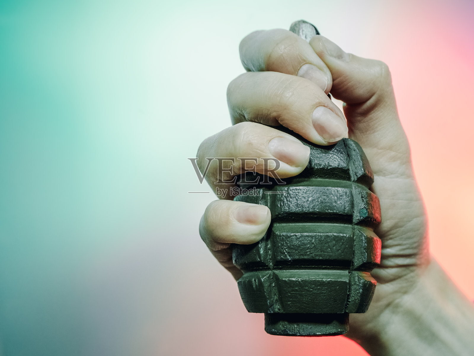 一张特写照片，一只手在多色背景上捏着一枚绿色的军事手榴弹。照片摄影图片