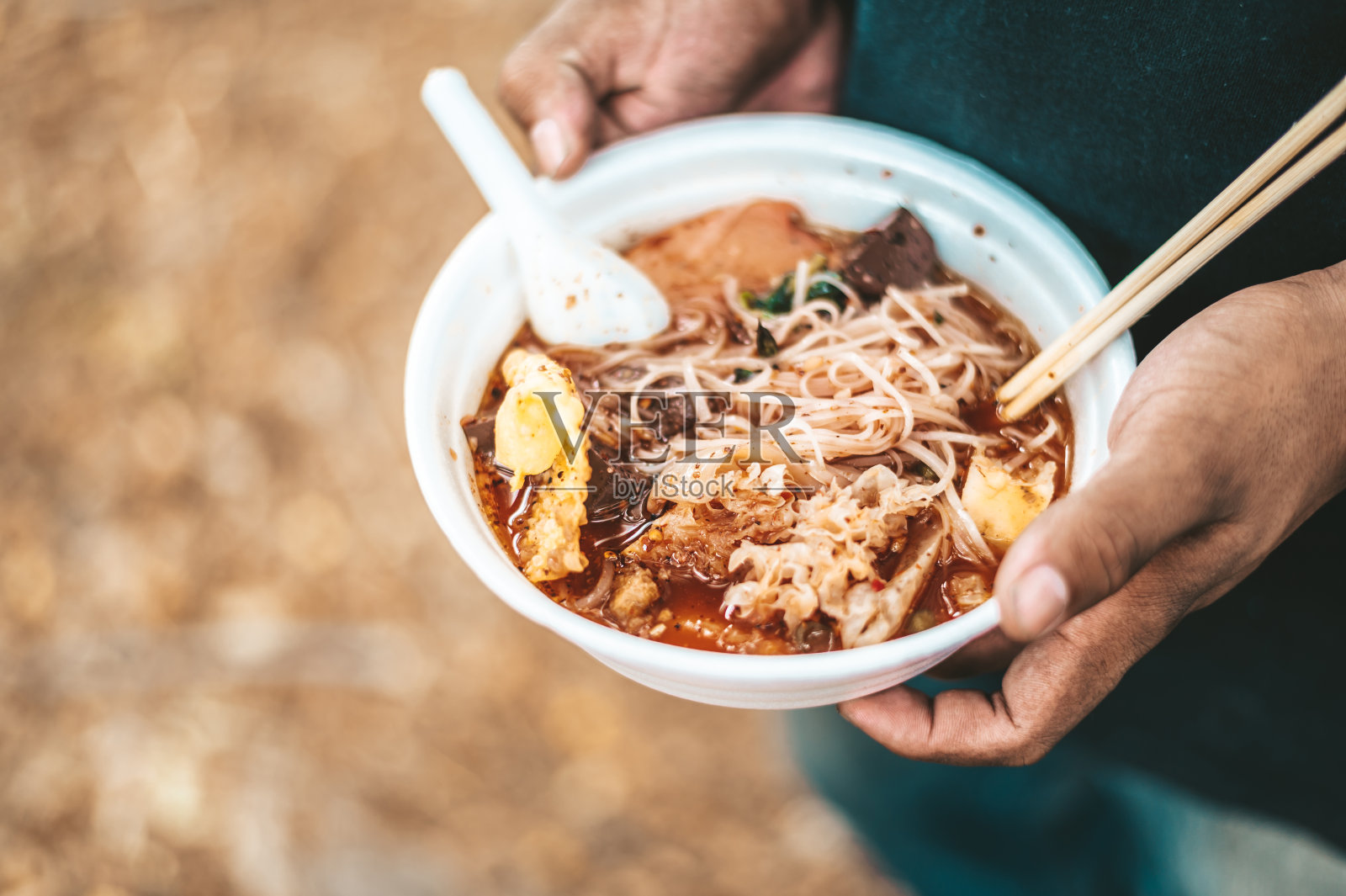 乞丐站在一个泡沫杯里拿着面条，还有筷子和勺子。照片摄影图片