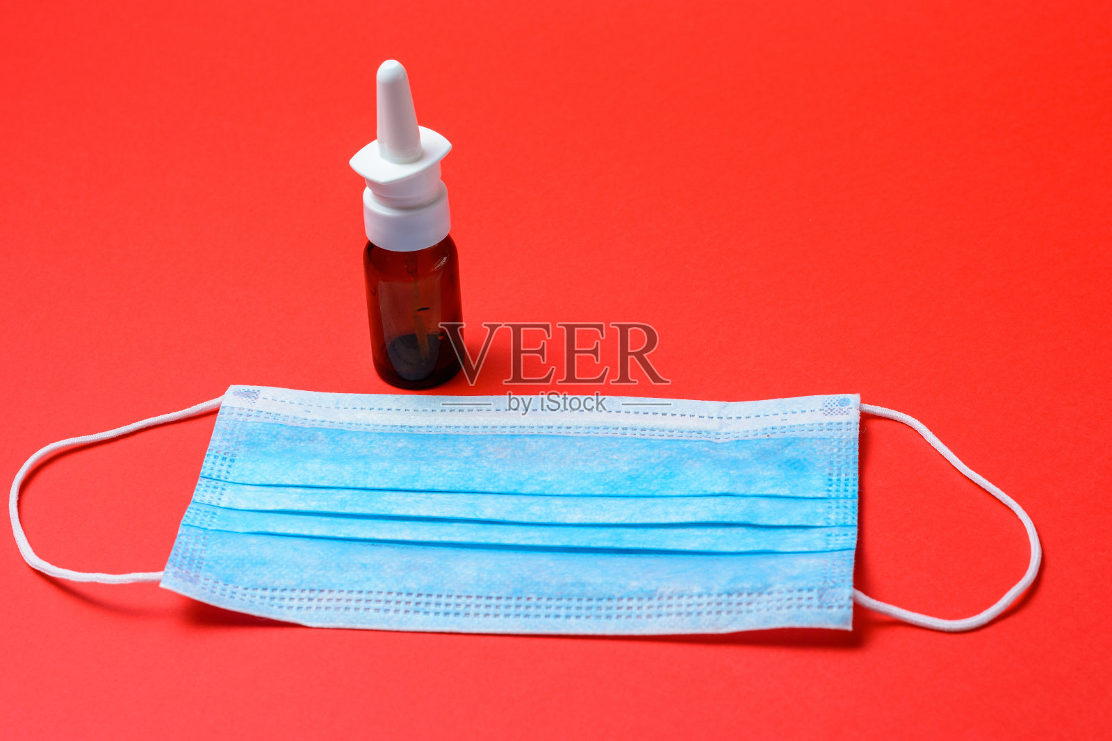红色背景上有一个治疗流鼻涕和过敏的瓶子，医用口罩。照片摄影图片