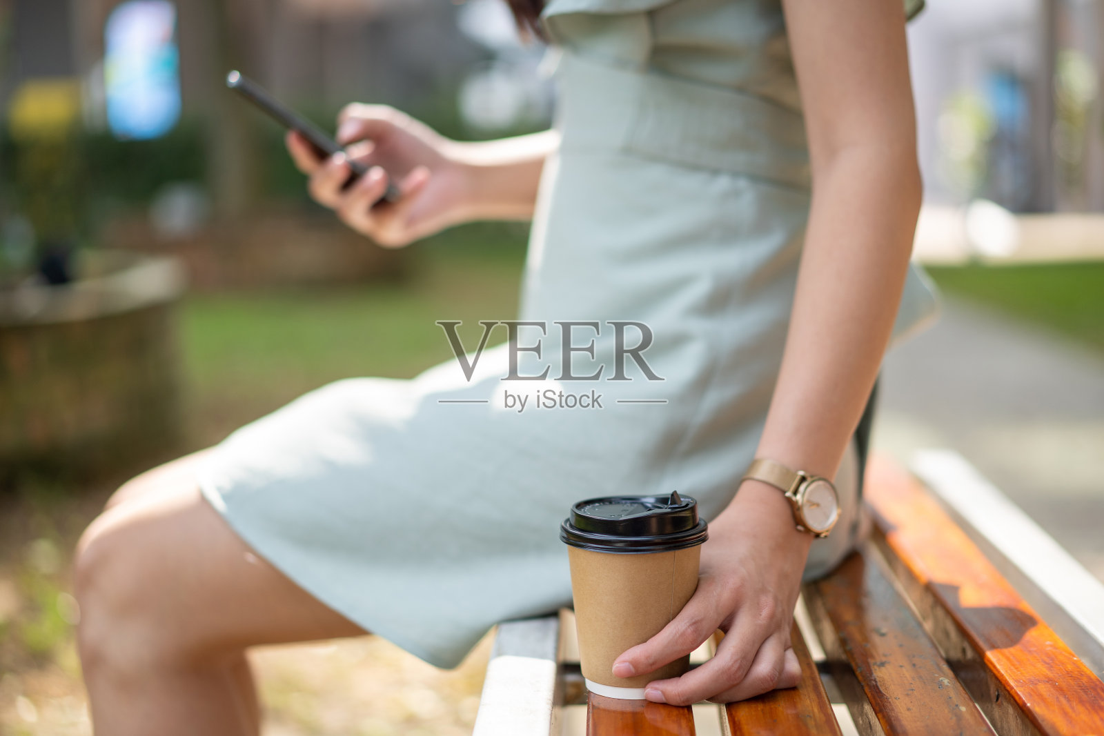 年轻的亚洲女人手拿着外卖咖啡，坐在长凳上照片摄影图片