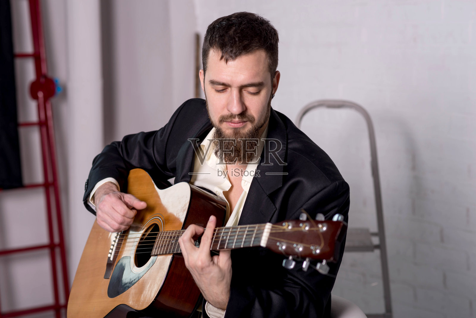 一个穿着衬衫和夹克的男人拿着一把木吉他特写。照片摄影图片