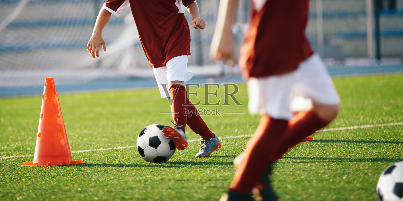 男孩们在训练筒之间踢足球。欧洲足球运动青年运动员夏令营。在草地上踢足球的男孩。背景是足球球门和体育场照片摄影图片