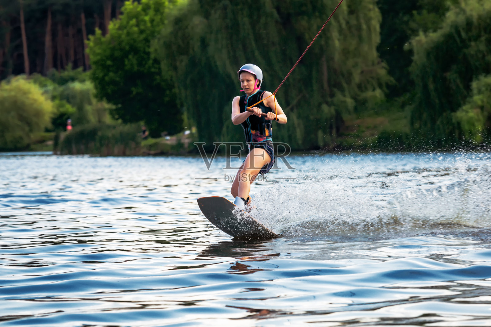 女人骑花式滑水。在夏日的湖中切浪溅起水花照片摄影图片
