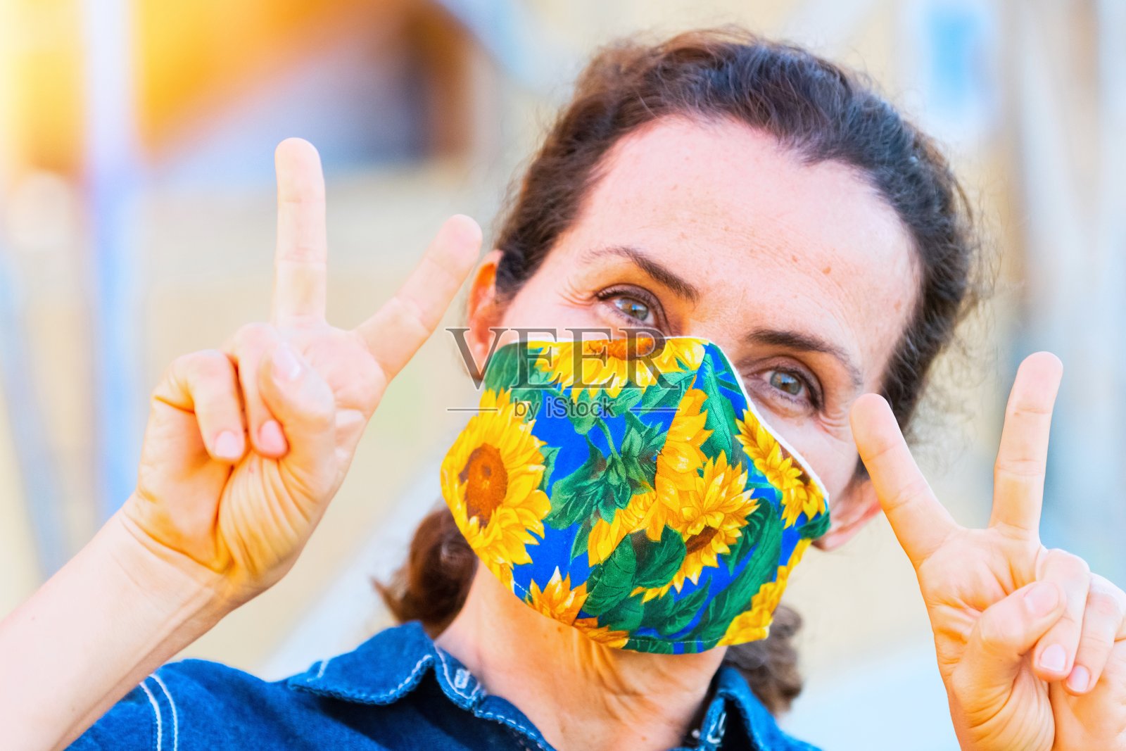 成熟的女人微笑着摆姿势，戴着色彩齐全的保护面罩，用手示意胜利照片摄影图片