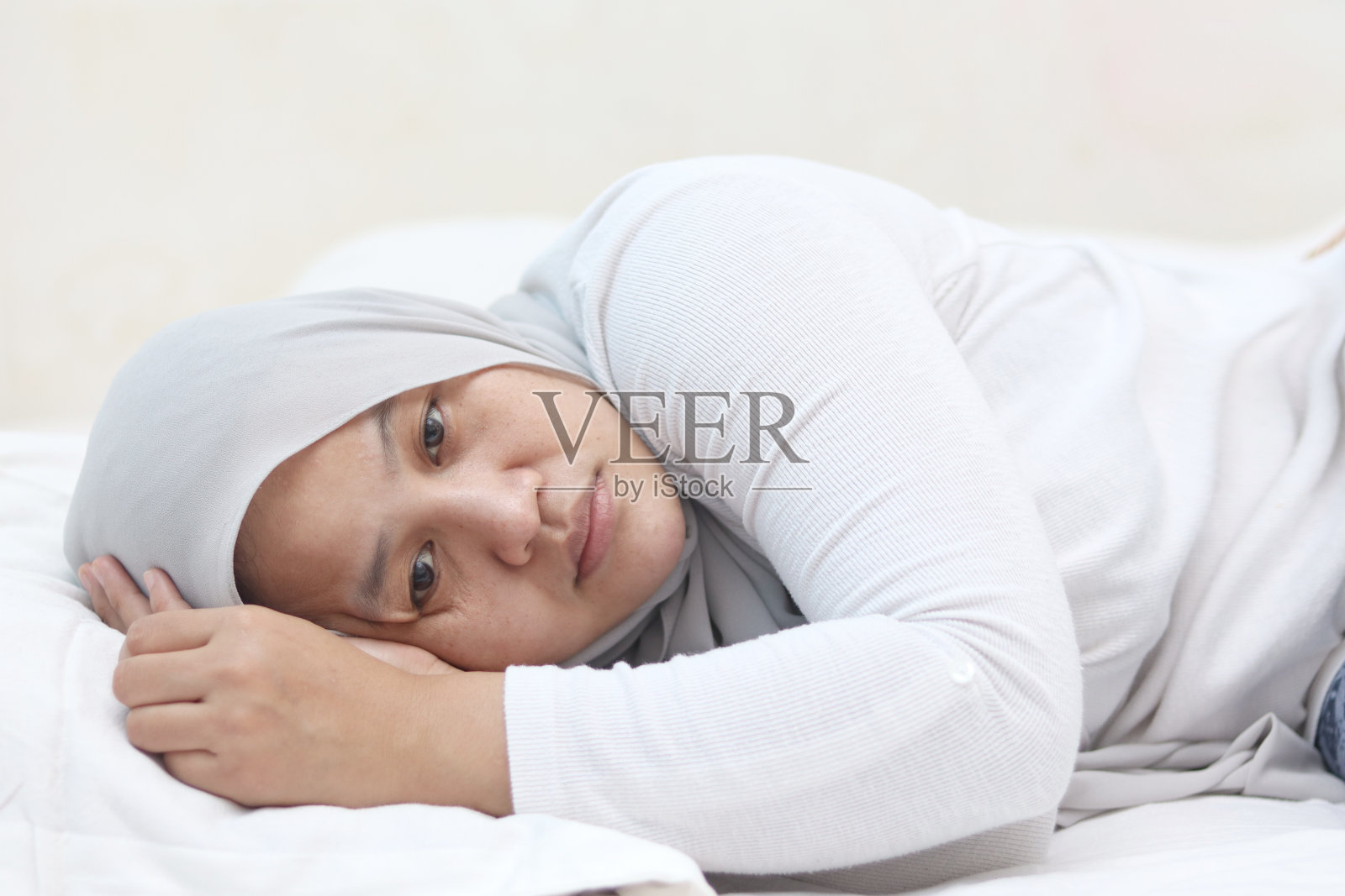 悲伤、不开心的亚洲穆斯林妇女躺在床上，目光呆滞，难以入睡，想到了糟糕的境况照片摄影图片