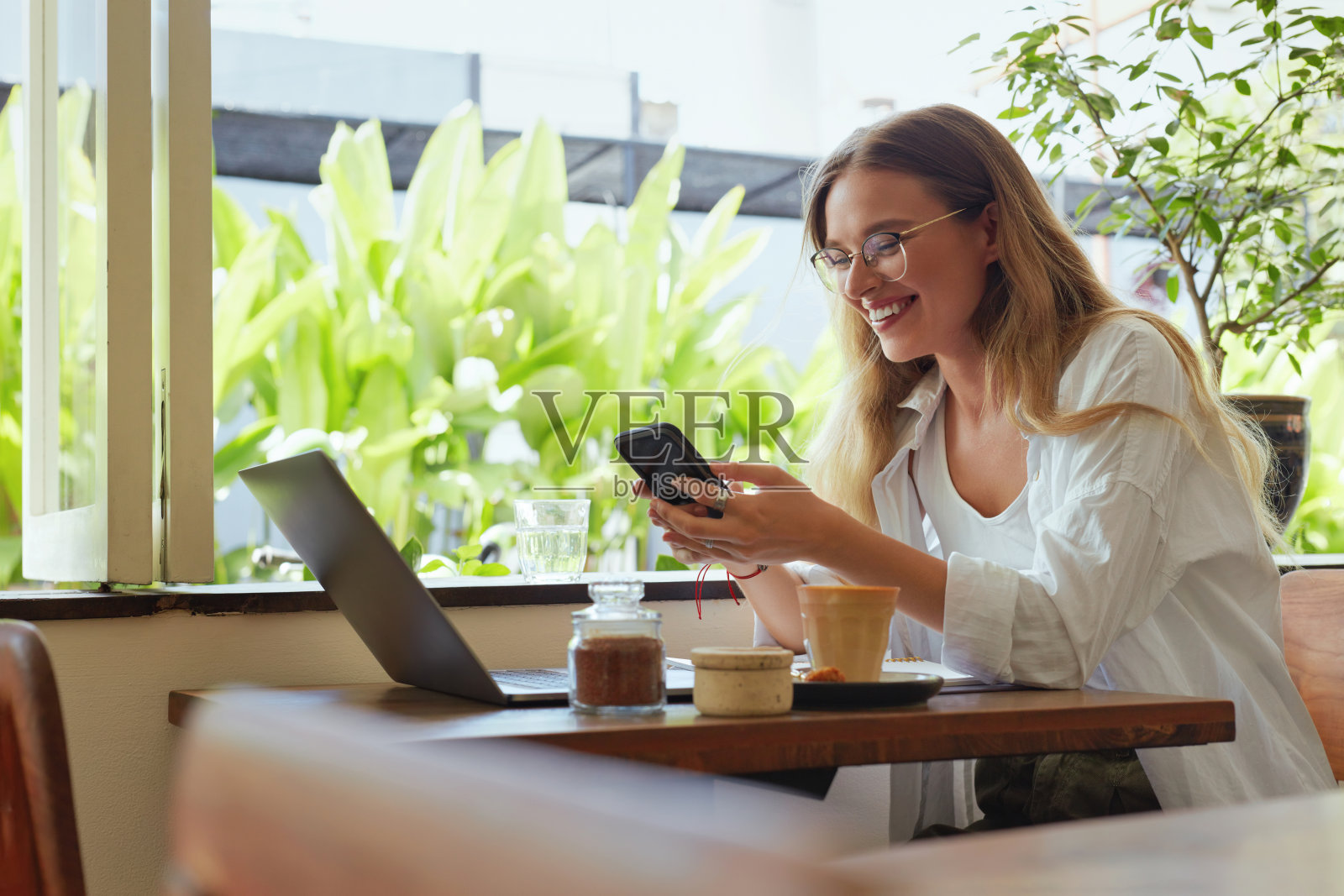 在线工作。女孩在咖啡馆用笔记本电脑和智能手机工作。美丽的商业女人在休闲衣服和眼镜肖像。工作，购物和学习的数字技术。照片摄影图片