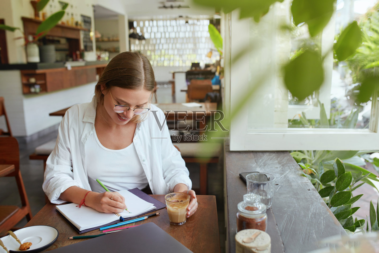 工作。在咖啡馆用笔记本电脑的女人。戴眼镜的时尚专注女孩在笔记本上写东西。在舒适的地方远程工作或学习的数字技术。照片摄影图片