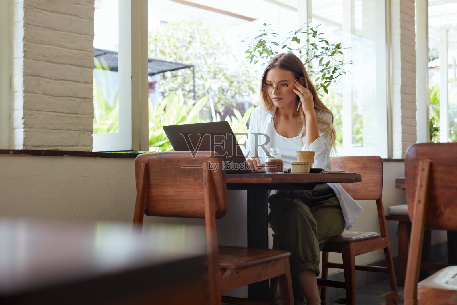 女人。在咖啡馆在线工作。穿着休闲装的漂亮女孩用笔记本电脑工作，触摸头部。现代数字技术远程工作或教育在舒适的工作场所。照片摄影图片