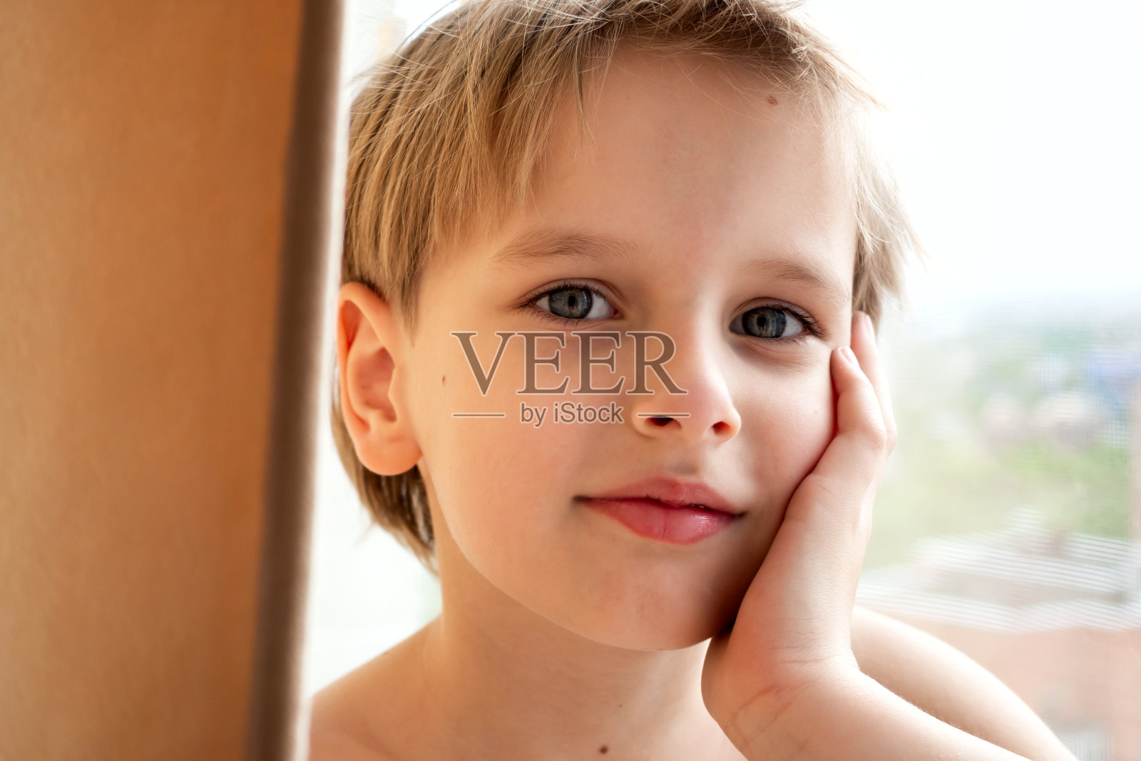 肖像年轻的白人可爱的男孩与金发在房子里靠近窗户。平静的情绪照片摄影图片