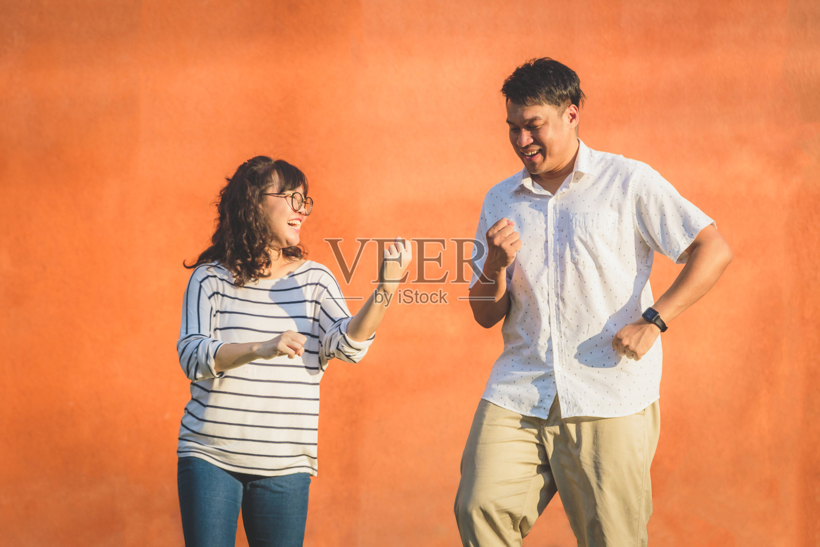 快乐的年轻亚洲夫妇的肖像一起大笑和跳舞在橙色的墙壁背景，夫妇放松和花时间在一起，人和生活理念照片摄影图片