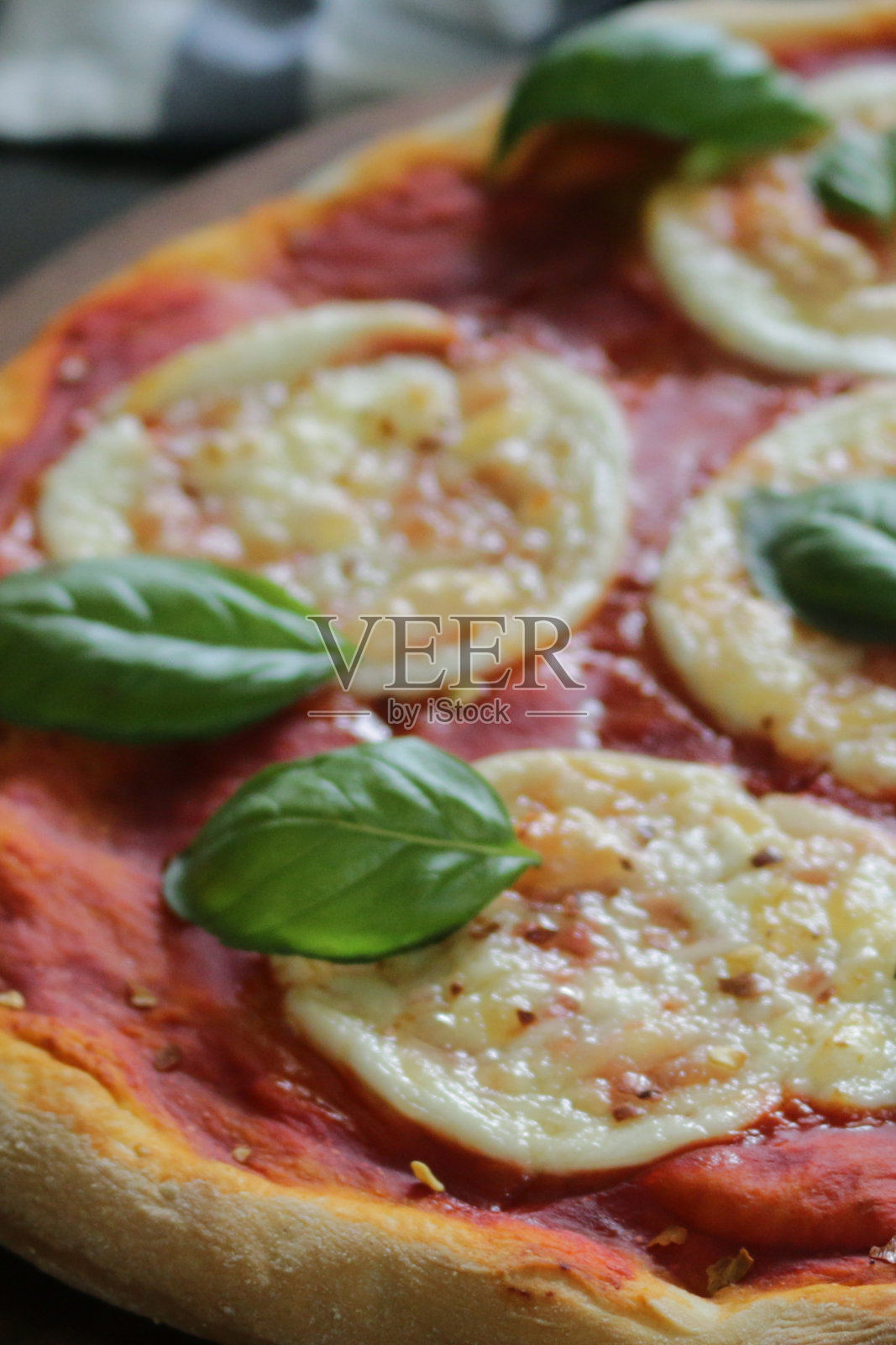 特写镜头:新鲜出炉的自制玛格丽塔披萨，金色的水牛马苏里拉奶酪圈，丰富的番茄番茄沙司和新鲜的罗勒叶，重点放在前景照片摄影图片