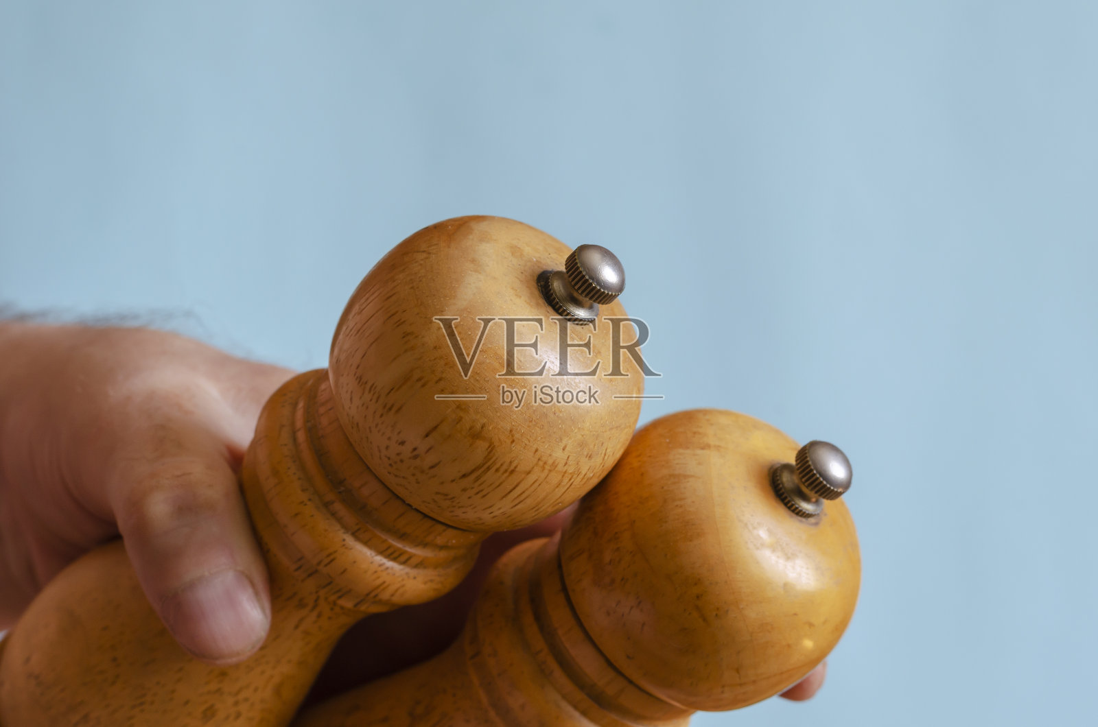 一个成年男子手里拿着两个木制胡椒磨。照片摄影图片