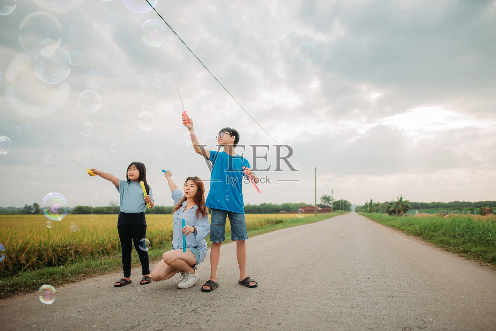 亚洲华人家庭花闲暇时间一起玩泡泡棒在乡村街道照片摄影图片