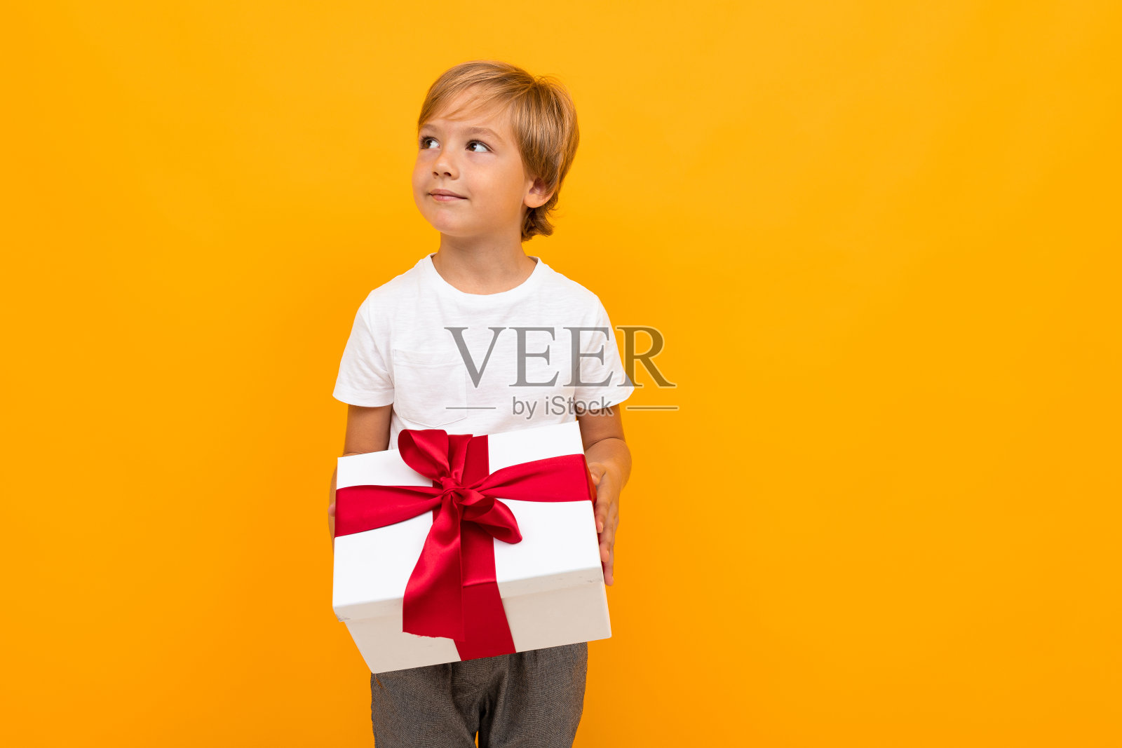 男孩拿着一个系着红丝带的盒子，看着远处橙色的背景照片摄影图片