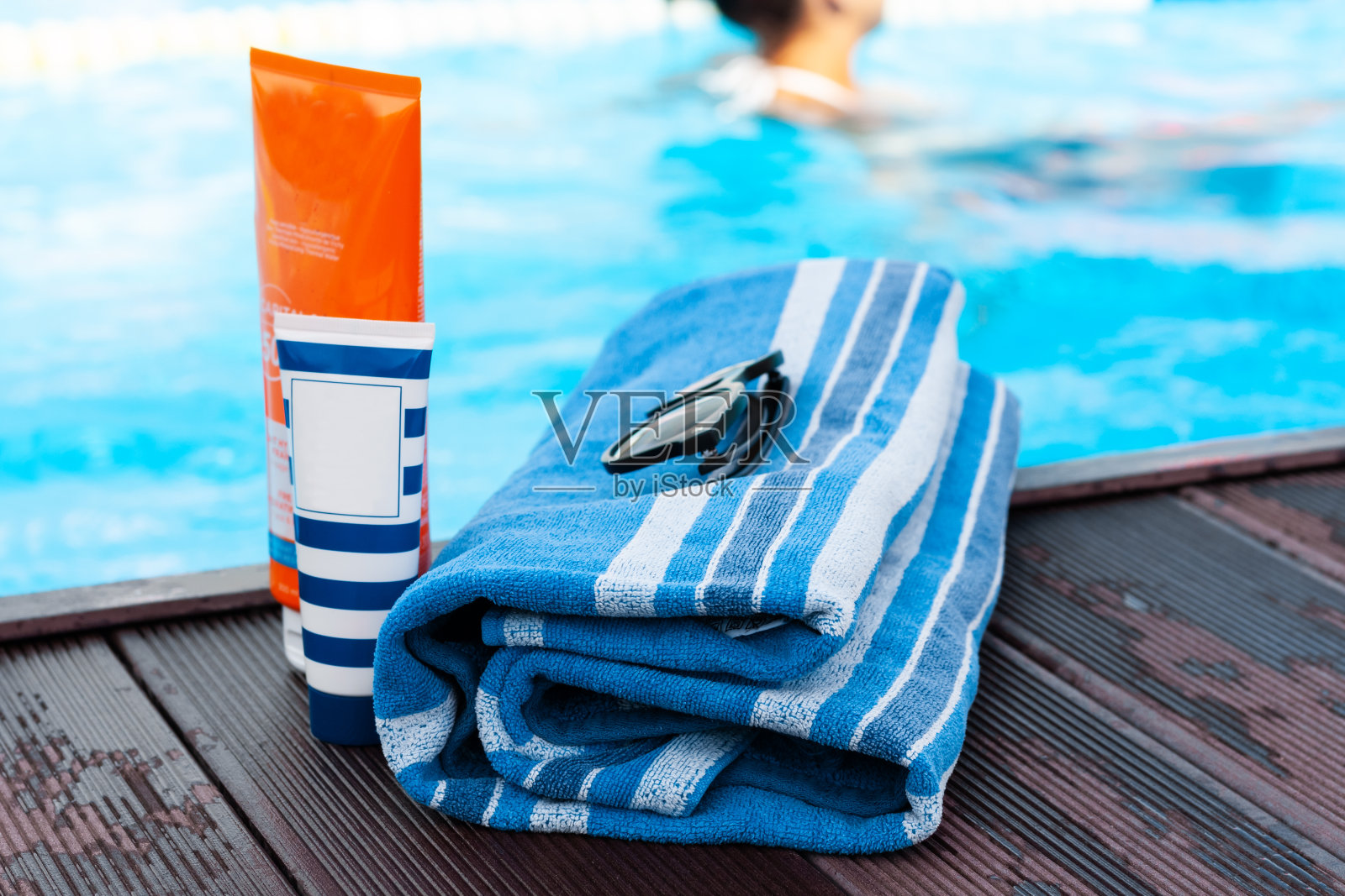 太阳眼镜，防晒霜管，游泳池附近的蓝色毛巾，热带背景照片摄影图片