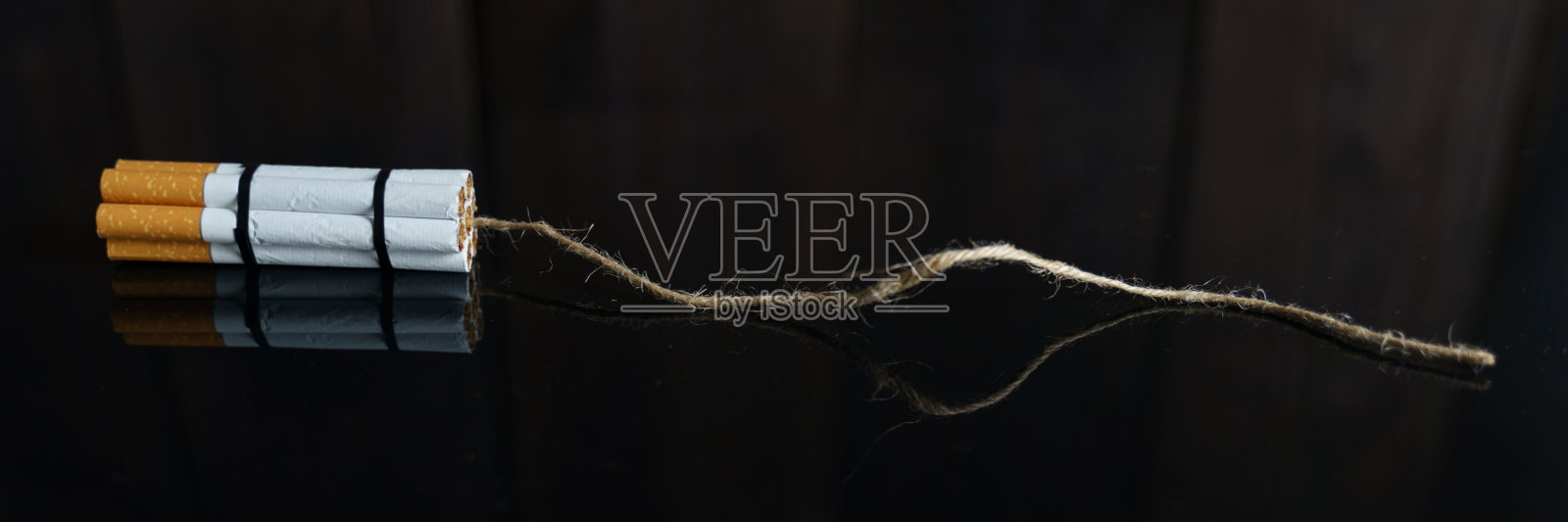 香烟被扭曲成一个炸药格子，在黑色的反光表面上有一根灯丝。照片摄影图片