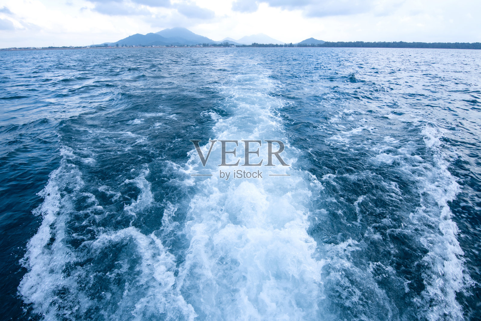 以岛屿为背景的船只后面的蓝色海面上的痕迹和泡沫波。照片摄影图片