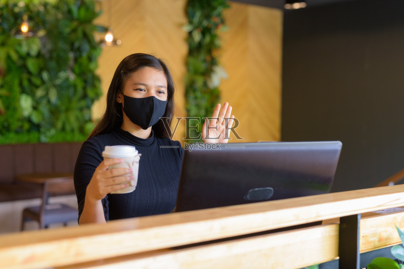 年轻的亚洲女商人戴着面具视频通话和坐在距离内的咖啡店照片摄影图片
