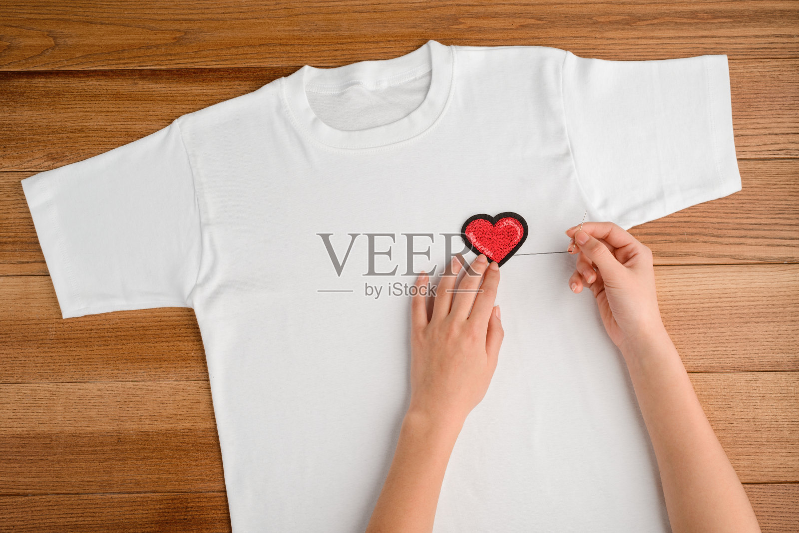 她正在白色t恤上缝心脏补丁，俯视图照片摄影图片