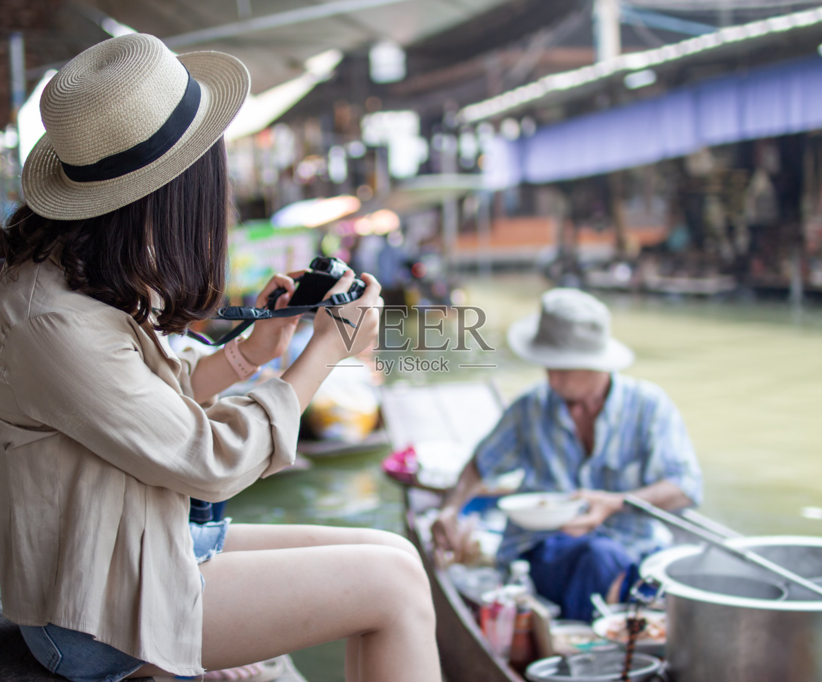 亚洲女性游客戴着帽子拿着相机和智能手机拍摄视频直播。美丽的女人乘坐出租船访问达姆努恩Saduak浮动市场，Ratchaburi。照片摄影图片