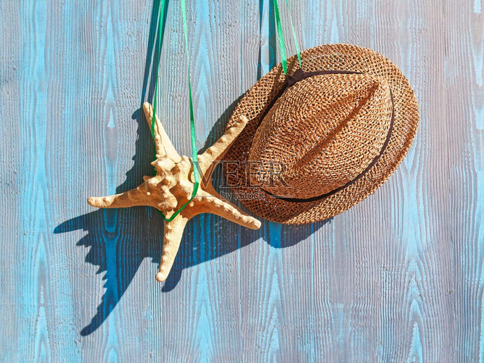 夏季背景，假期概念。草帽和海星挂在绿色的丝带上，蓝色的木头背景。照片摄影图片
