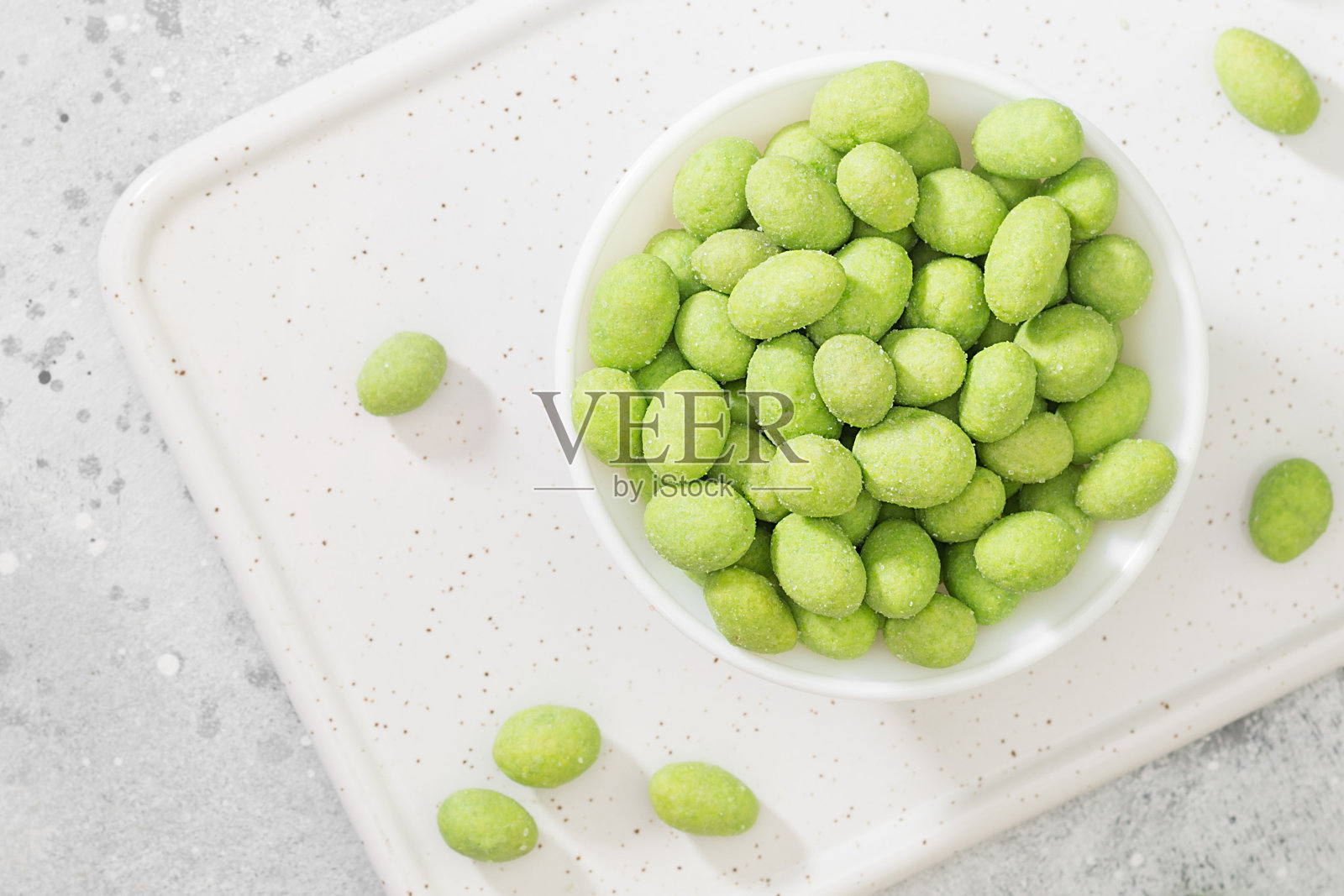 浅灰色的桌子上，白色的碗里放着芥末炒花生。近距离看芥末花生照片摄影图片