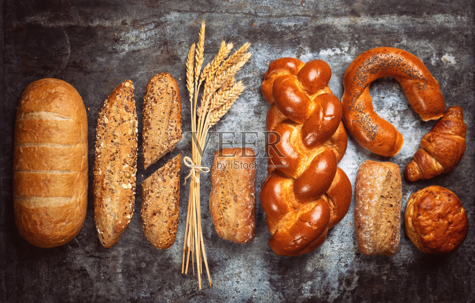 新鲜烘焙的食物。粗糙的餐桌背景上有混合面包和小面包的硬面包和小麦穗。俯视图和复制空间为您的广告文本信息。照片摄影图片