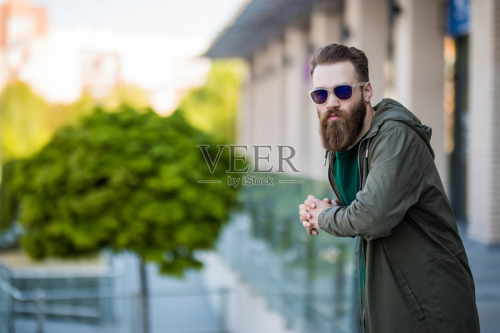 年轻的潮男留着胡子，戴着太阳镜，穿着夹克在街上摆造型照片摄影图片