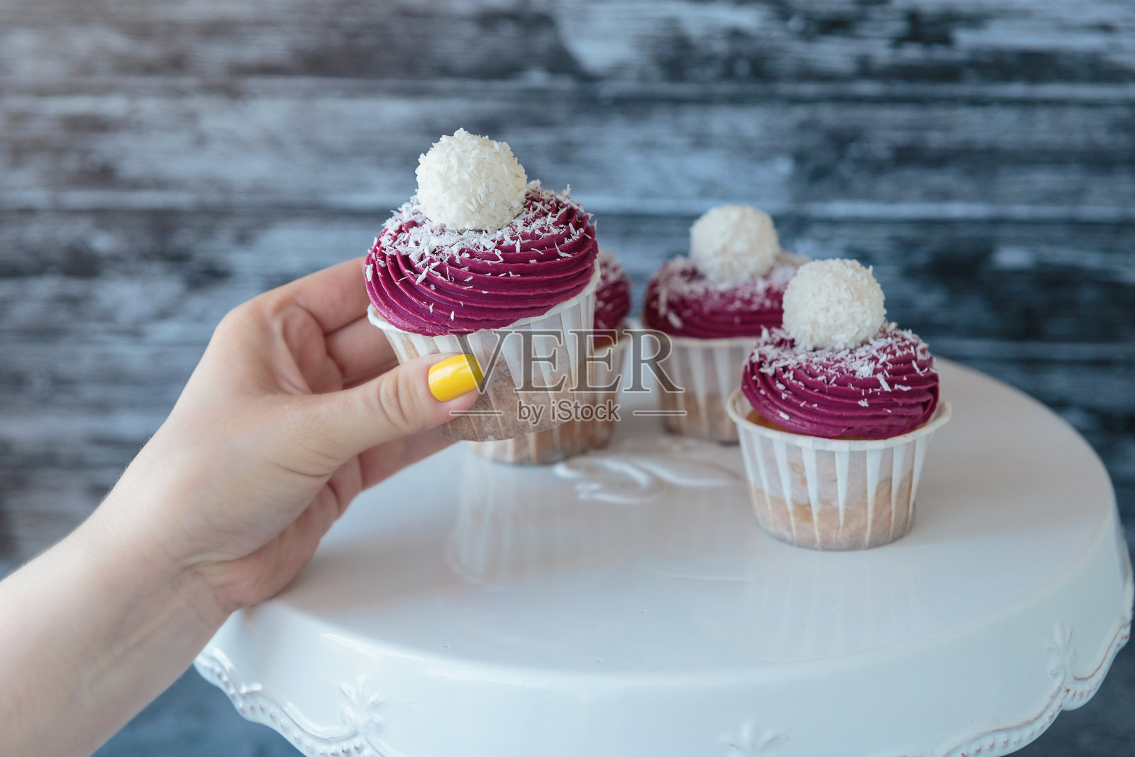 一位女士从小摊上拿了一个美味的纸杯蛋糕，白色的奶油装饰着球，上面有椰子屑，灰色的背景。照片摄影图片