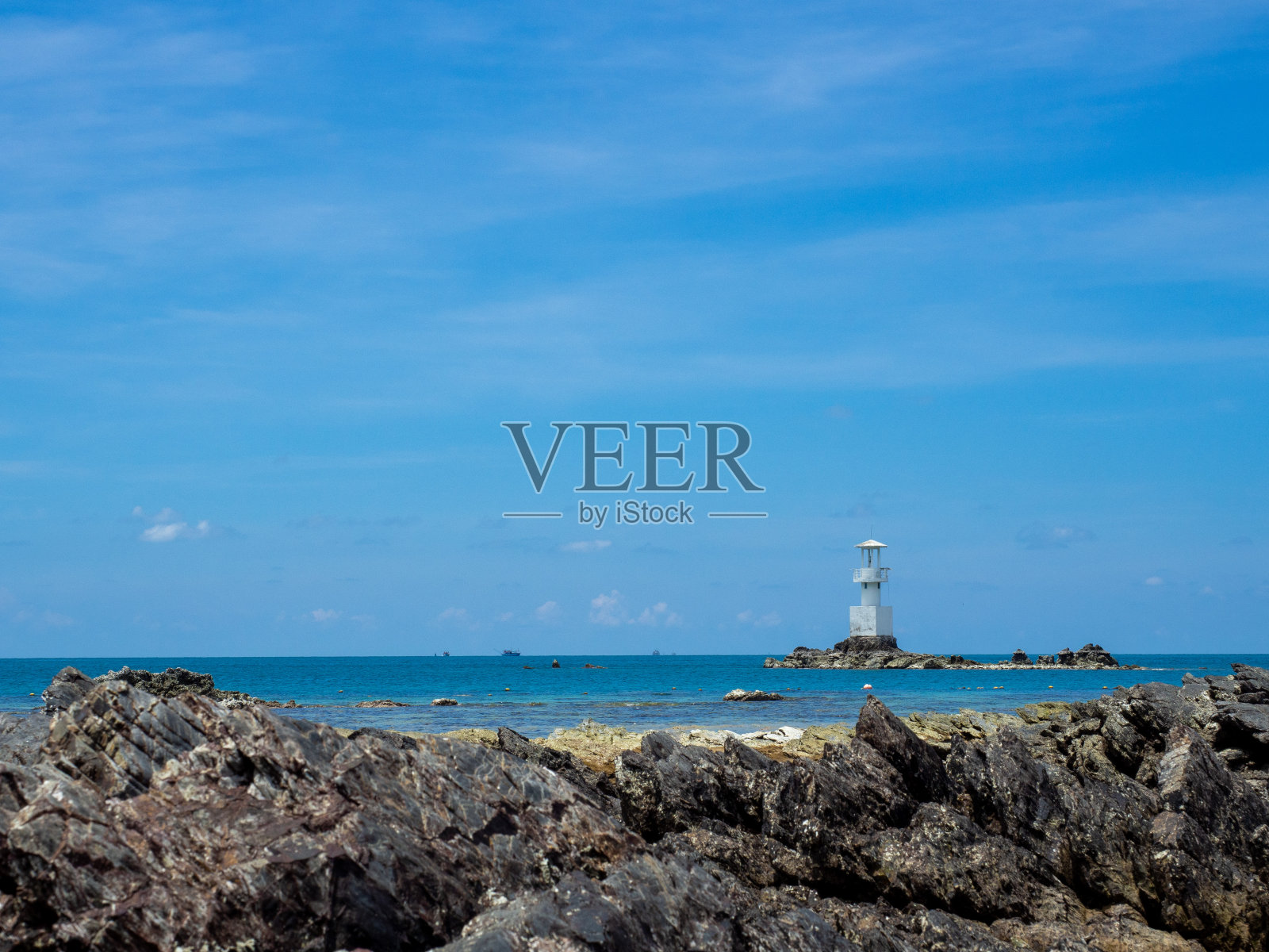 灯塔在明媚的夏日泰国海。前面是失去焦点的岩石海岸。照片摄影图片