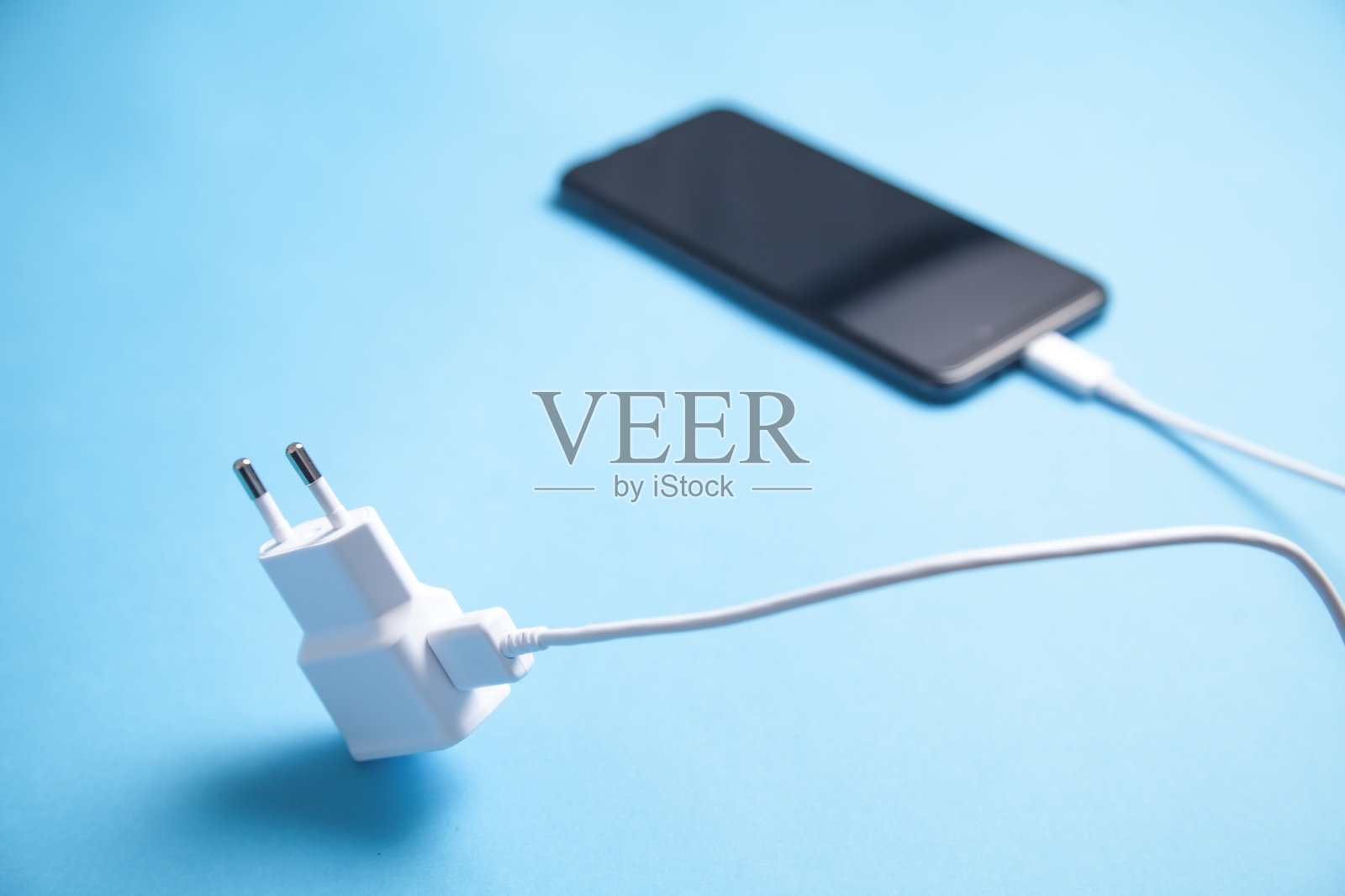 蓝色背景上有充电器的智能手机。照片摄影图片