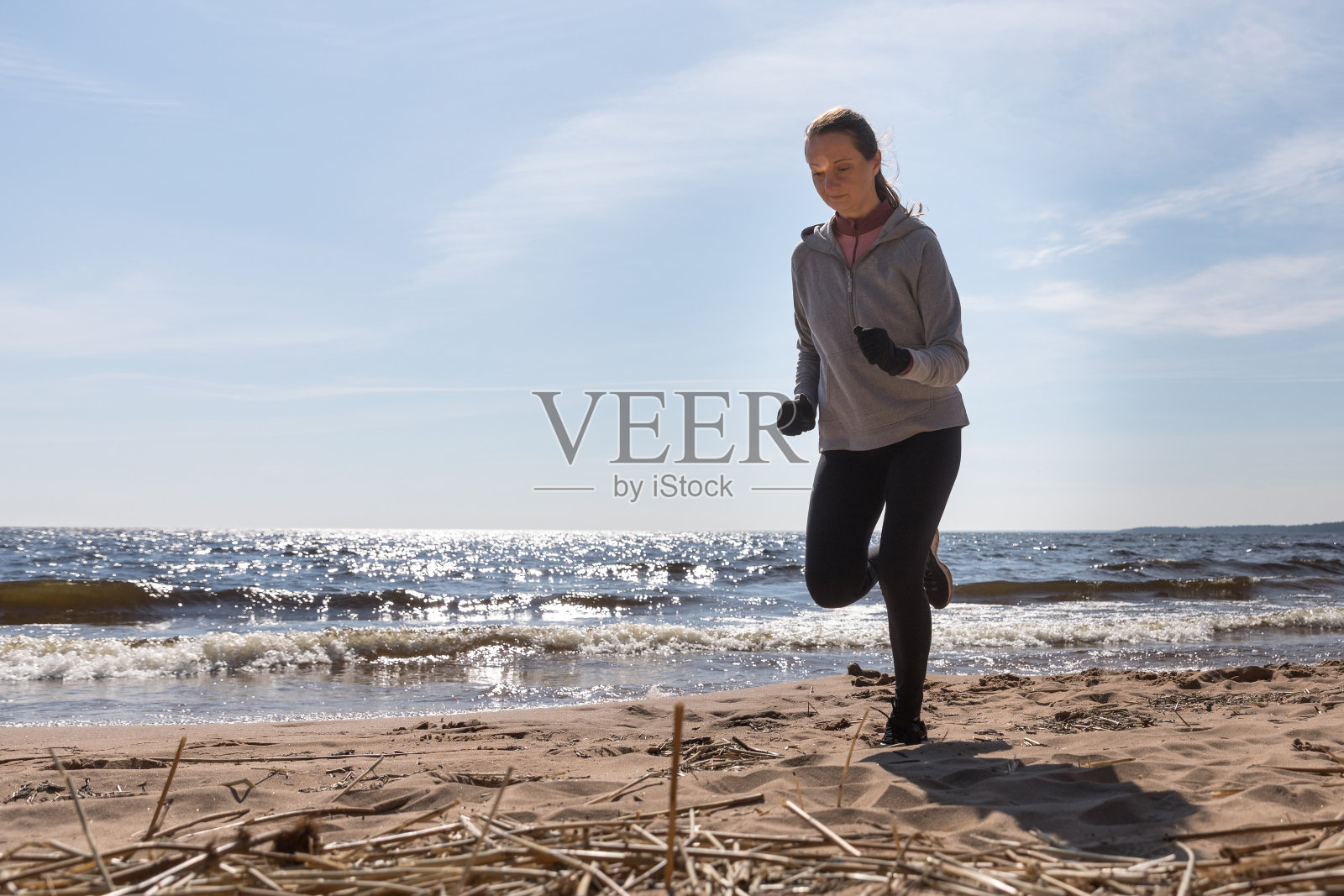 那个女孩正在海滩上从事运动。在沙滩上迎着水奔跑，运动员的剪影照片摄影图片