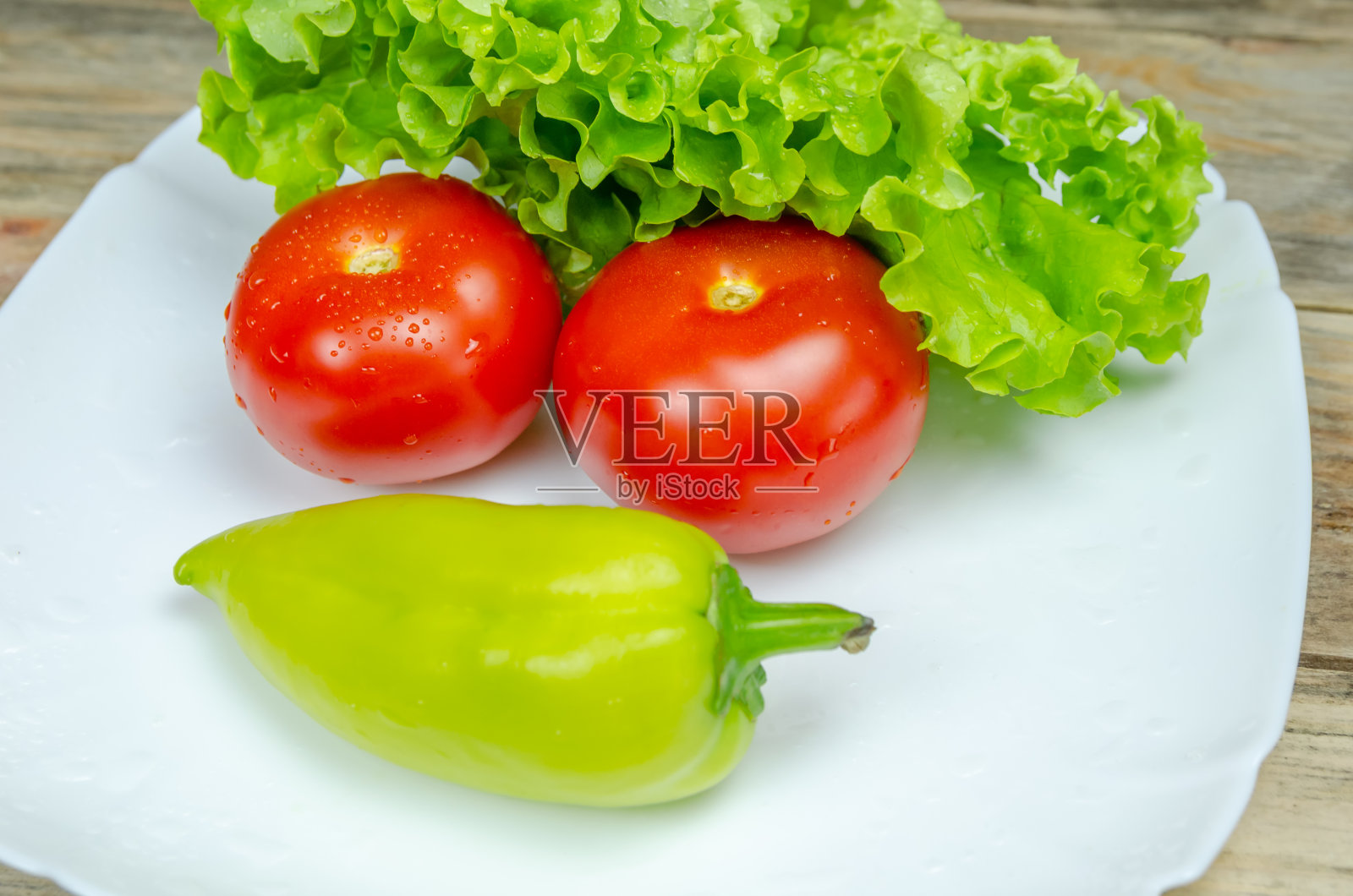 新鲜多汁的蔬菜辣椒，西红柿，黄瓜，生菜的叶子和水滴漂亮地摆放在一个白色盘子上特写。蔬菜以鬼脸的形式出现照片摄影图片