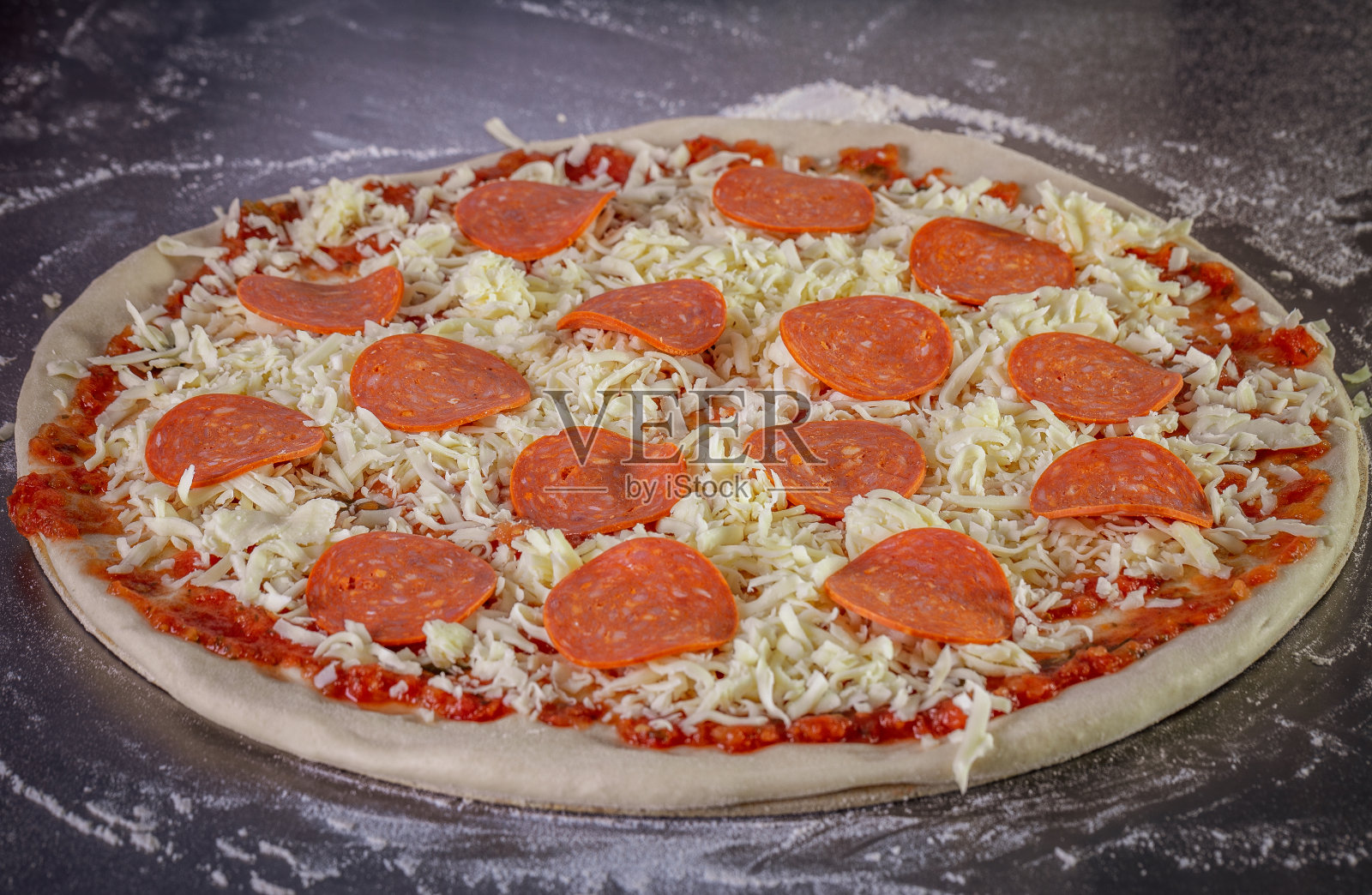 新鲜的披萨面团，配以番茄酱、马苏里拉奶酪和意大利辣香肠。制作披萨的过程照片摄影图片