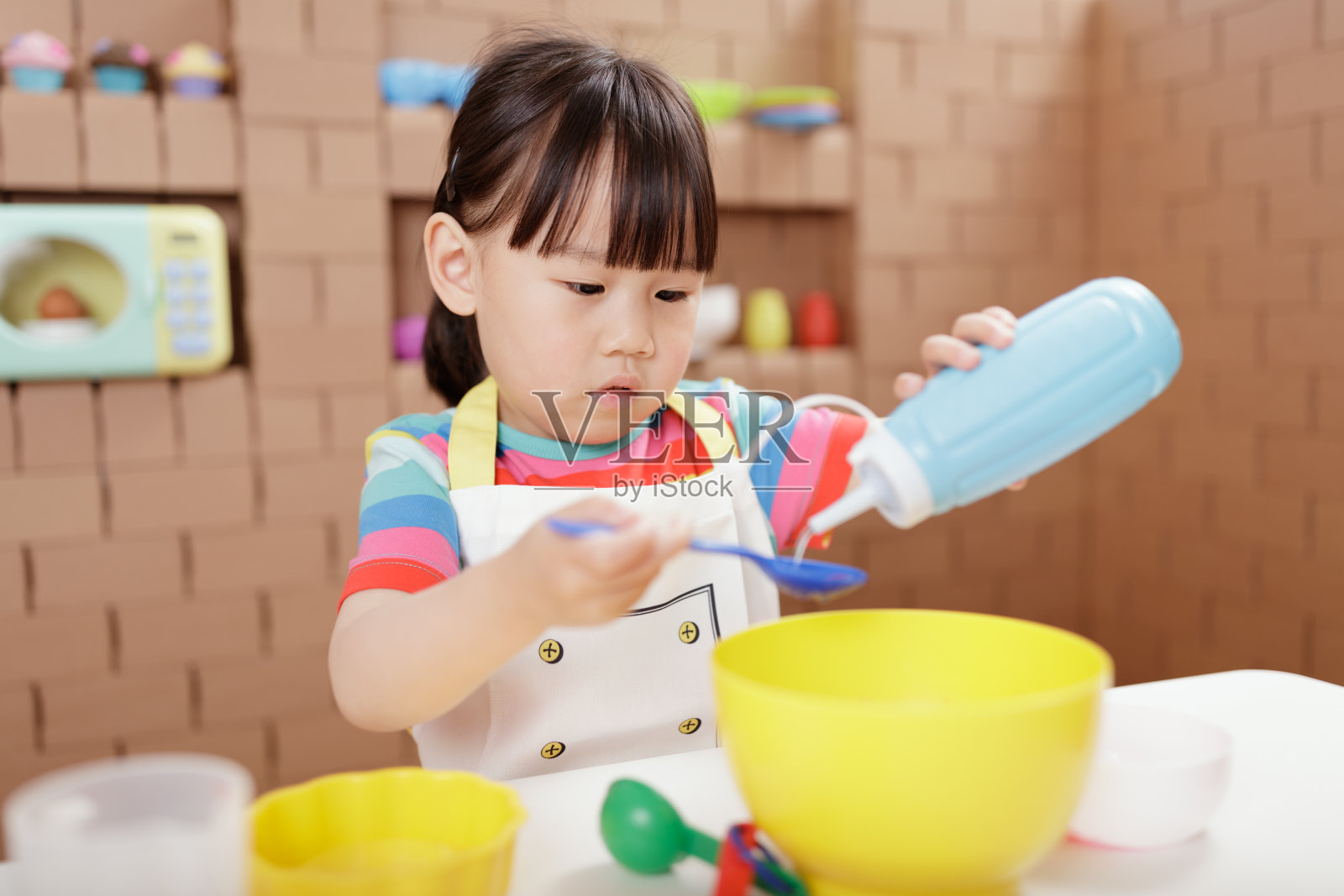 蹒跚学步的小女孩以纸板店为背景，假装扮演准备食物的角色照片摄影图片