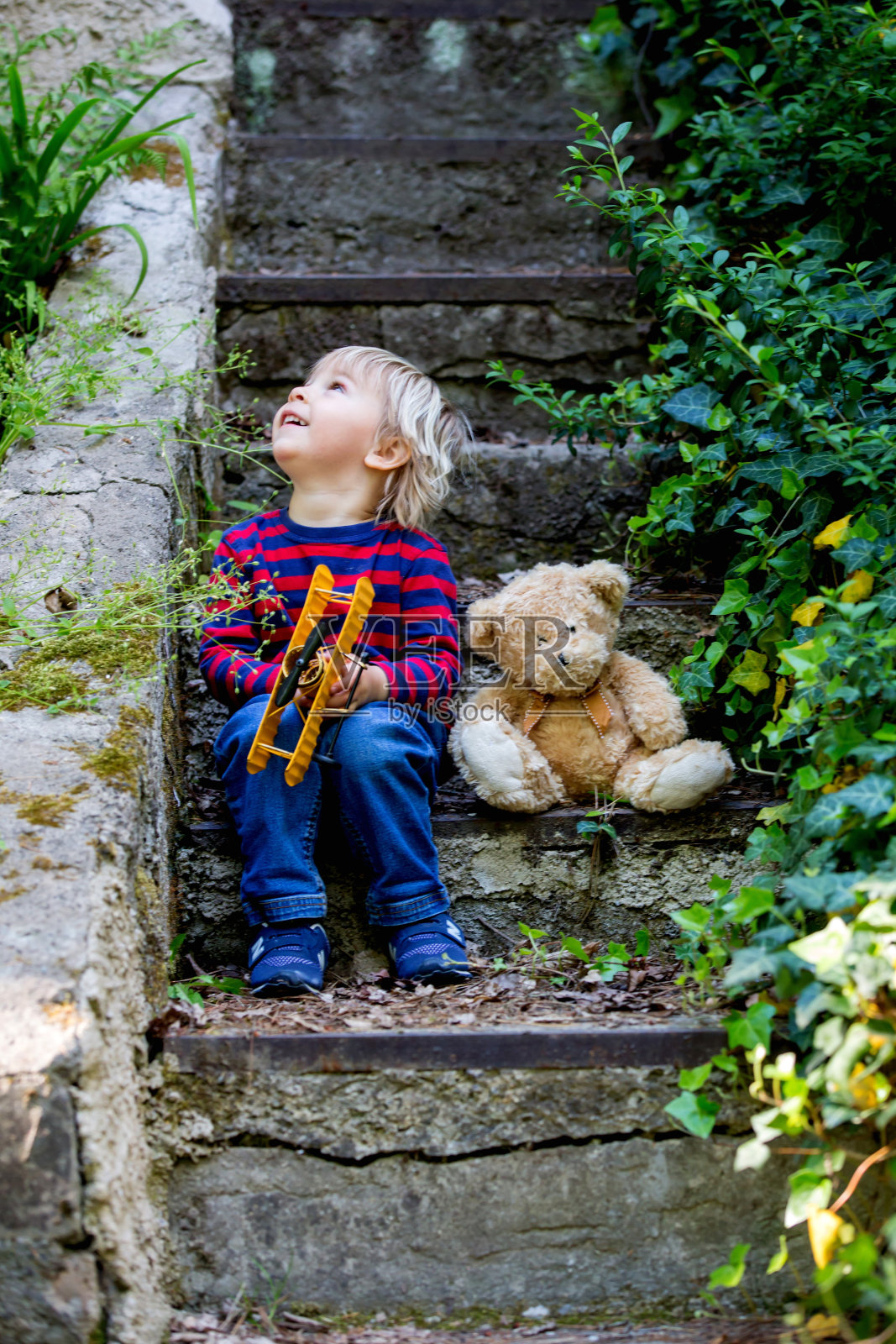 可爱的蹒跚学步的小男孩，和泰迪熊坐在楼梯上照片摄影图片