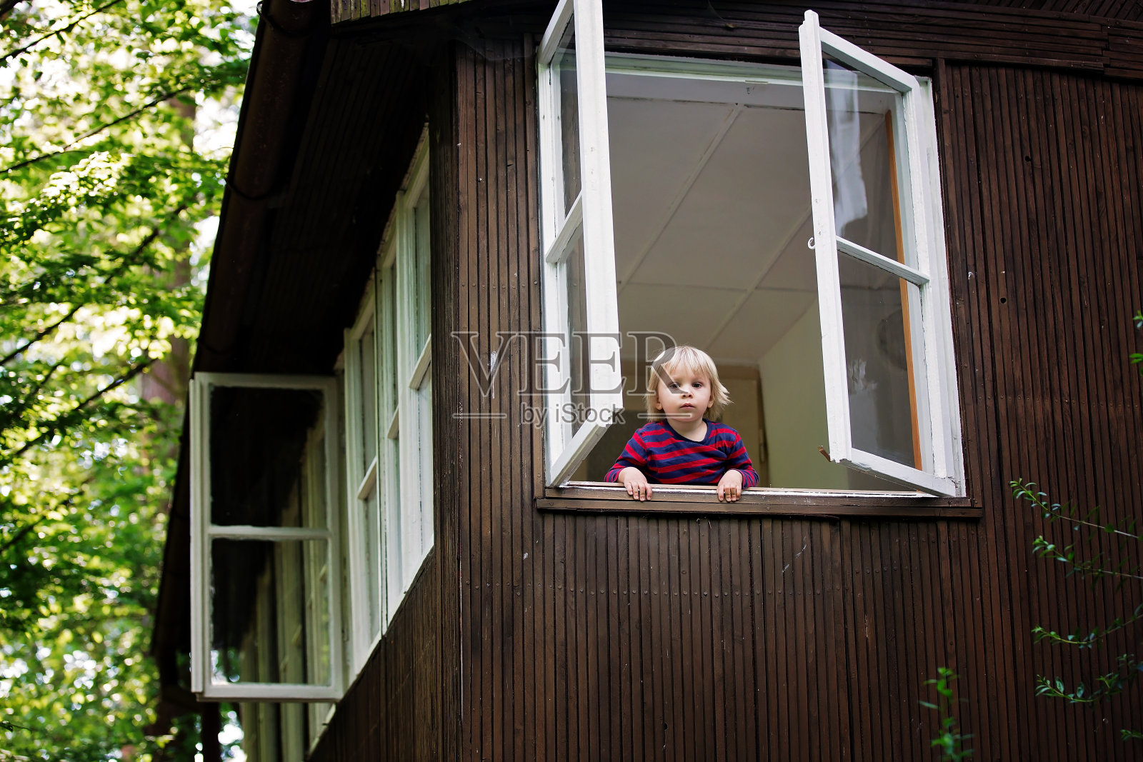 可爱的蹒跚学步的小男孩，看着窗外的小木屋在树林里照片摄影图片
