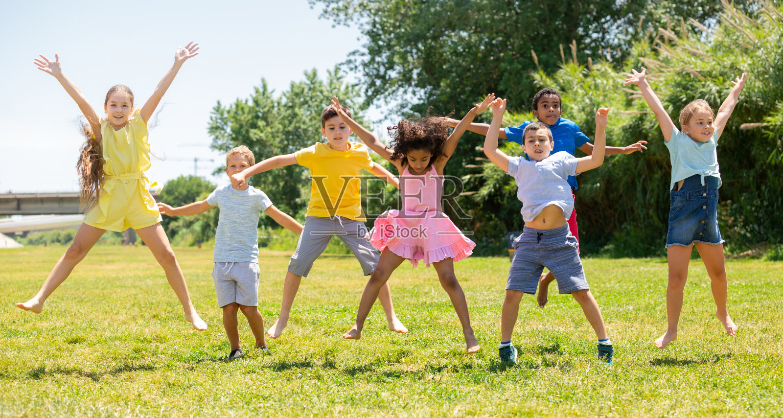 快乐的学校孩子们在公园的绿色草坪上跳跃照片摄影图片