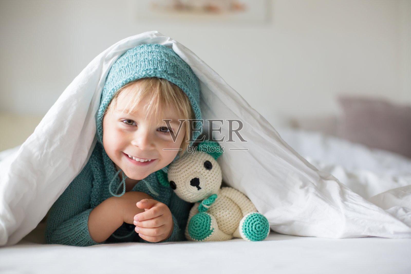 可爱的小男孩拿着手工编织的玩具，躺在床上照片摄影图片