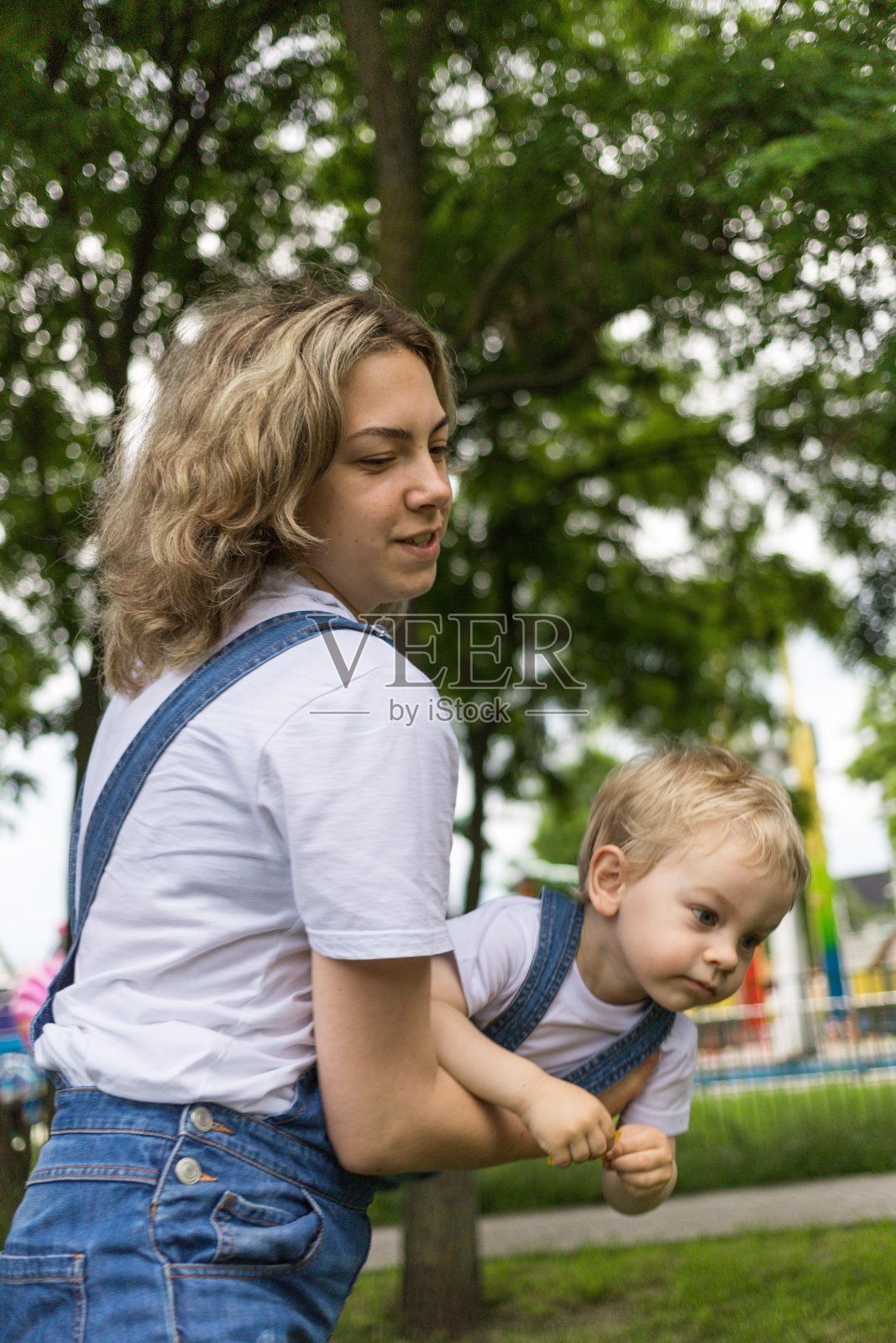 妈妈和儿子穿着一模一样的牛仔连衣裤在公园里散步。他们享受在一起的时光，彼此相爱照片摄影图片