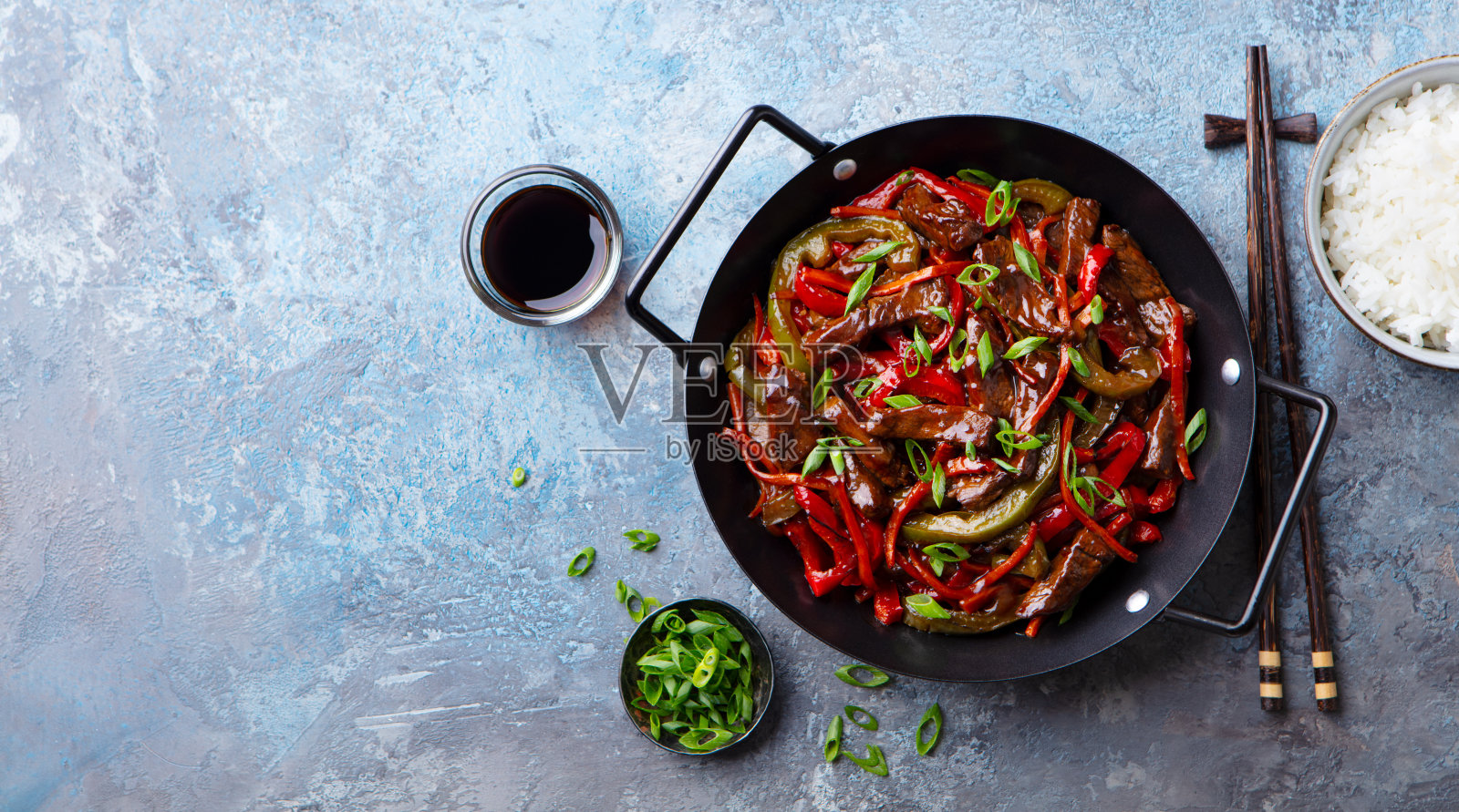 牛肉和蔬菜在平底锅里炒和米饭。蓝石头背景。副本的空间。前视图。照片摄影图片