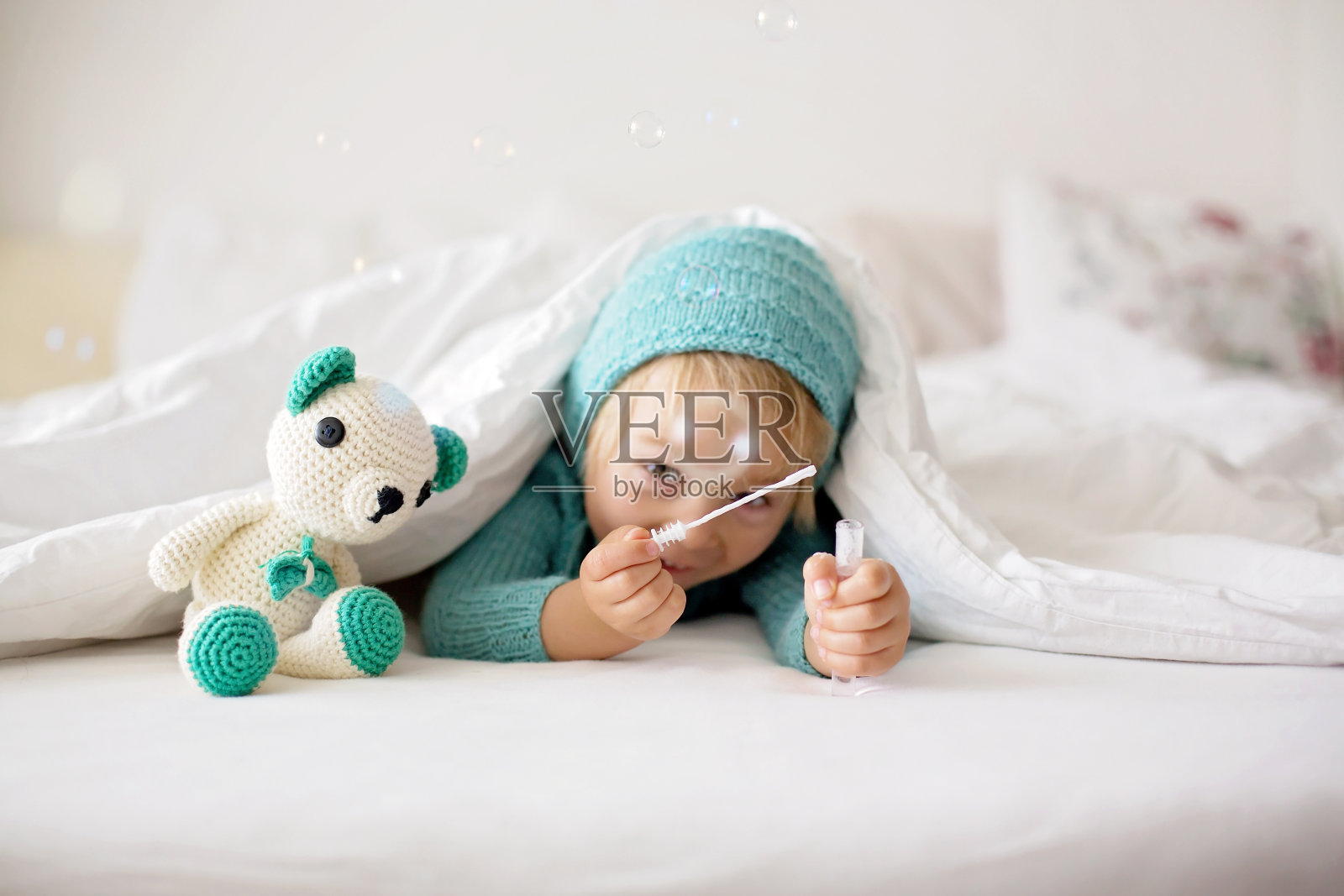 可爱的小男孩拿着手工编织的玩具，躺在床上照片摄影图片