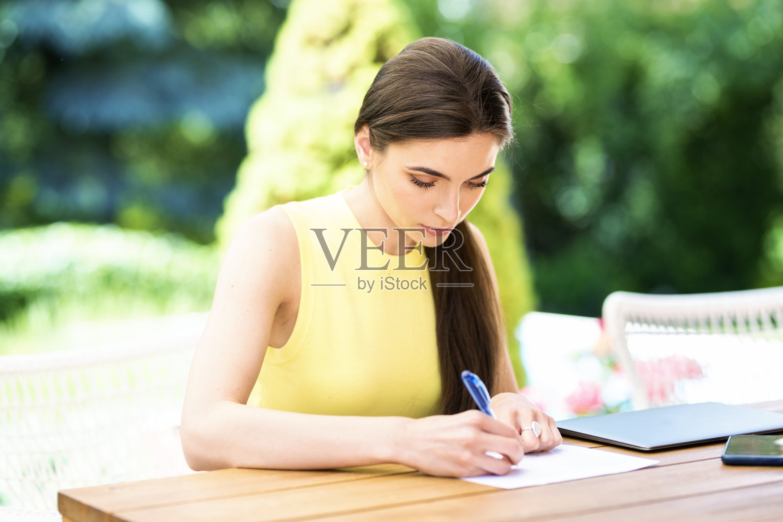 有魅力的年轻女子坐在阳台的书桌上，用钢笔在纸上写东西照片摄影图片