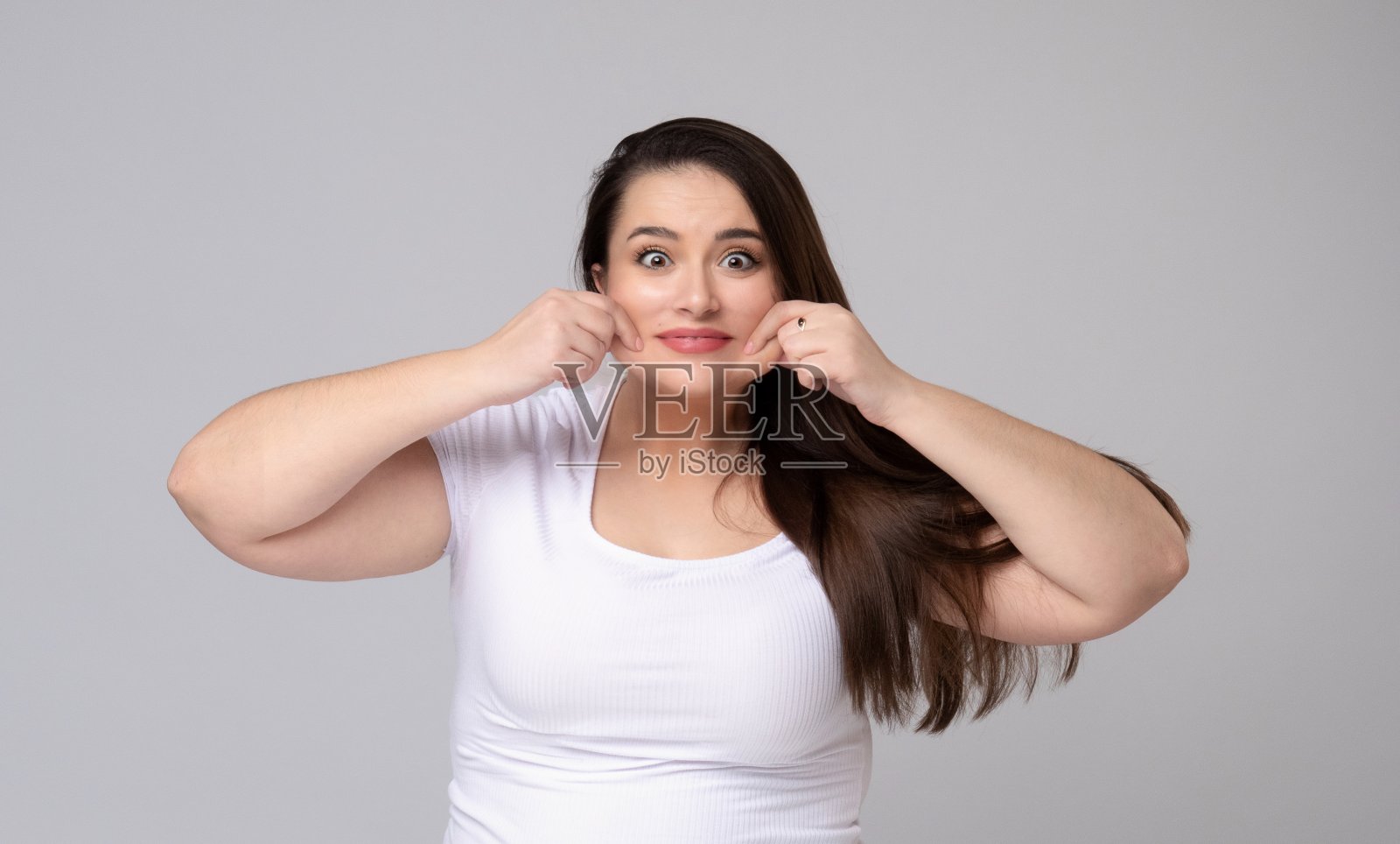 长头发的大尺寸模特扮鬼脸，拉着她的脸颊。照片摄影图片