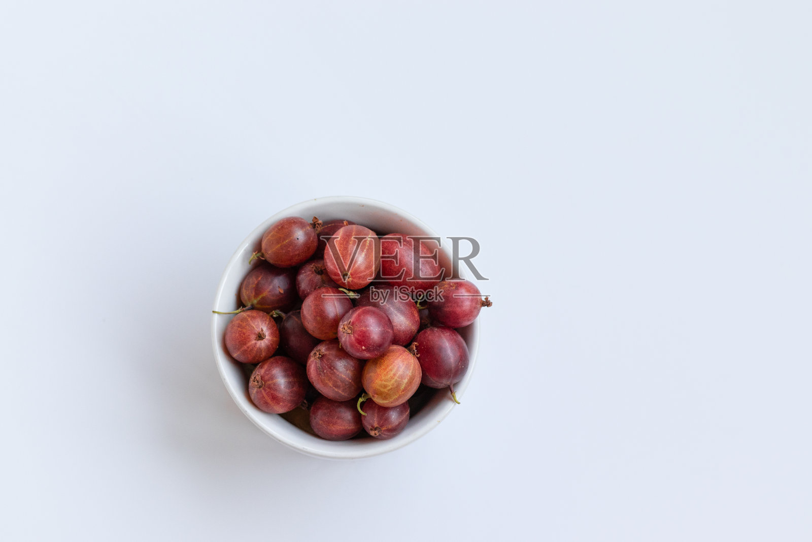 白色的桌子上，陶瓷碗里装着新鲜的醋栗。从以上观点。照片摄影图片