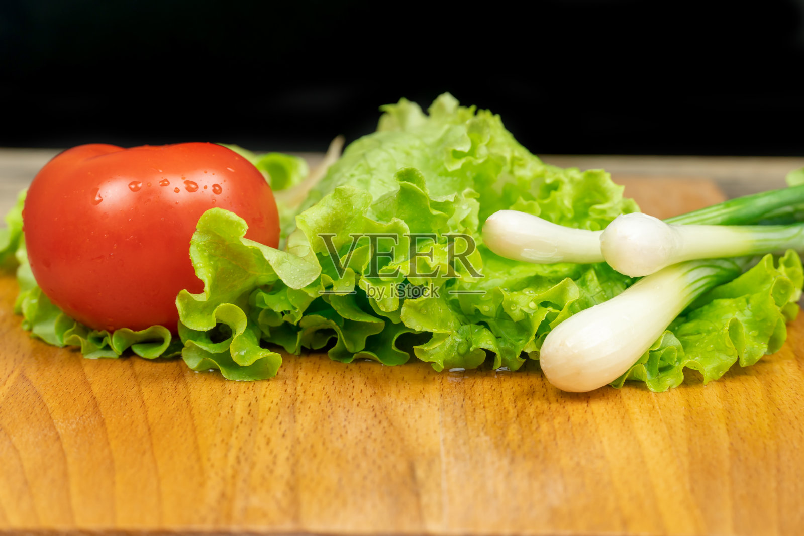 绿色的莴苣叶，番茄，绿洋葱与水滴在木板上，黑色的背景，复制空间照片摄影图片