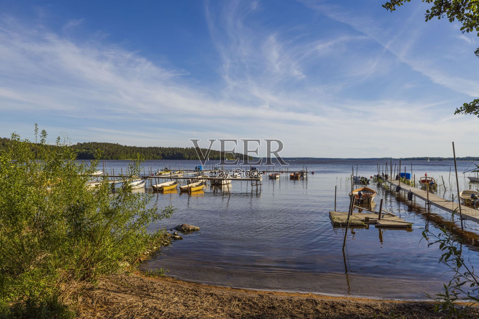夏日美丽的自然水景。停泊在湖岸的木船。绿树蓝天，白云为背景。瑞典。欧洲。照片摄影图片