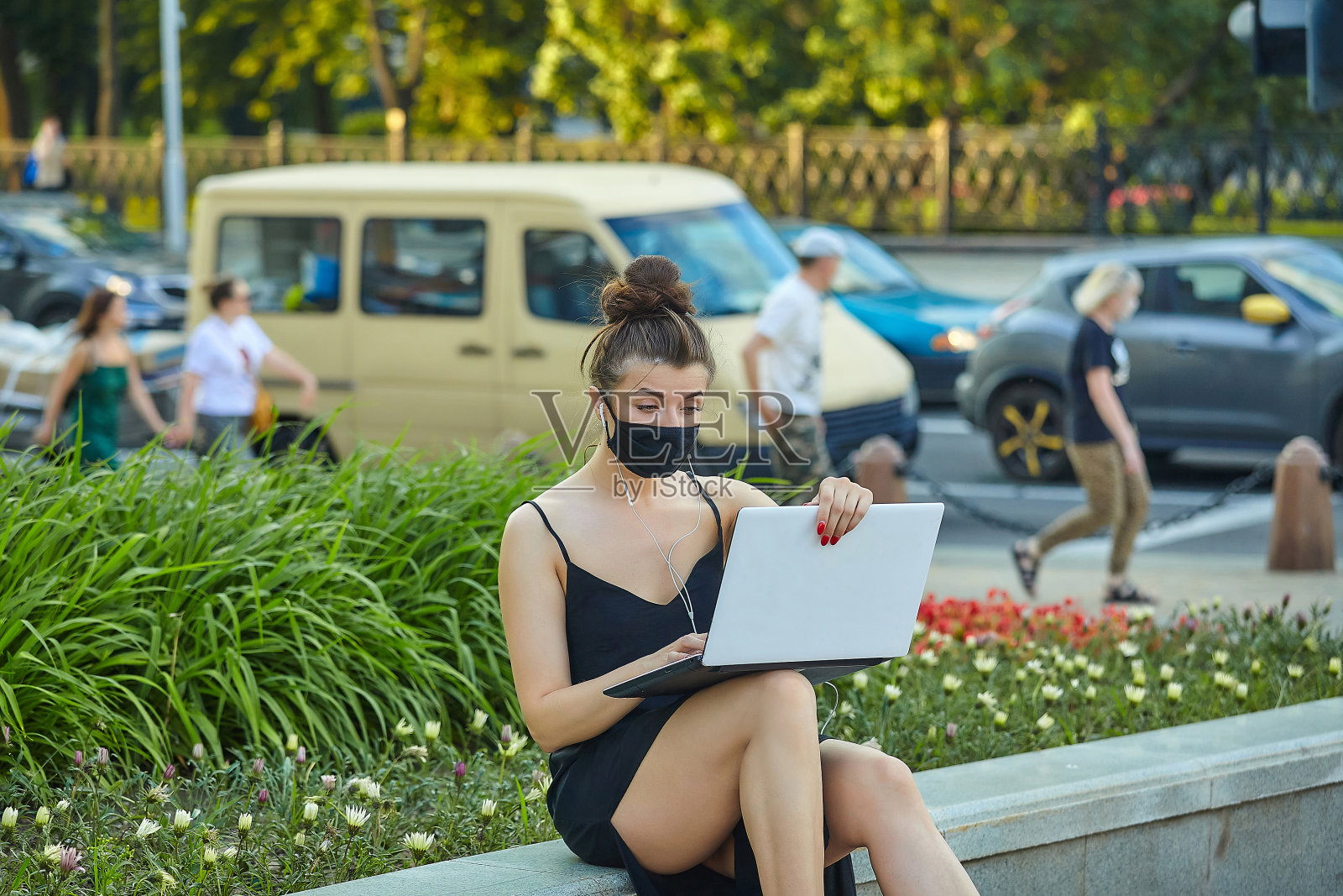 戴着面具的漂亮女孩在城市里走来走去，用笔记本电脑工作。拿着笔记本电脑听着音乐照片摄影图片