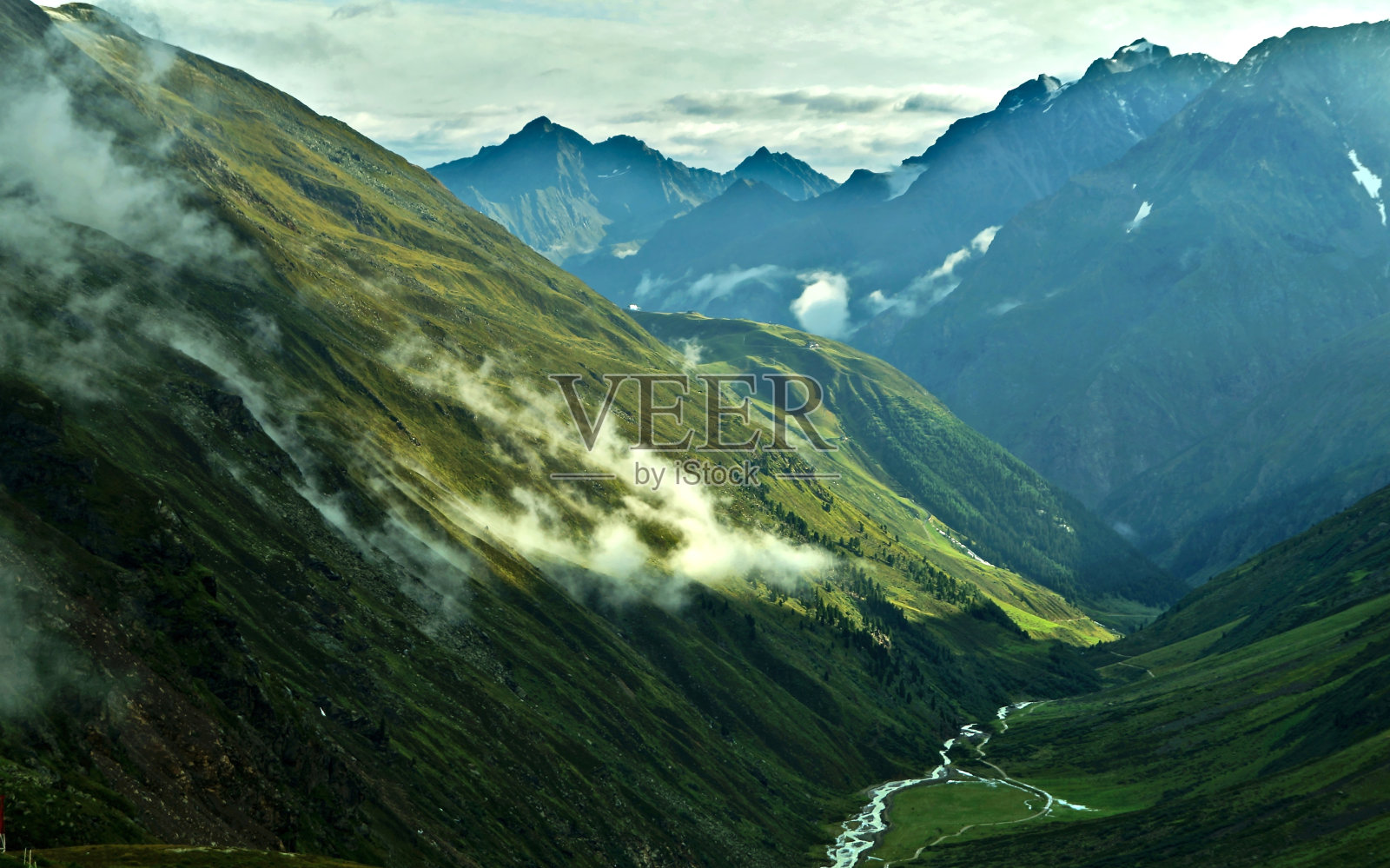山谷里有绿色的草地，云和高山照片摄影图片